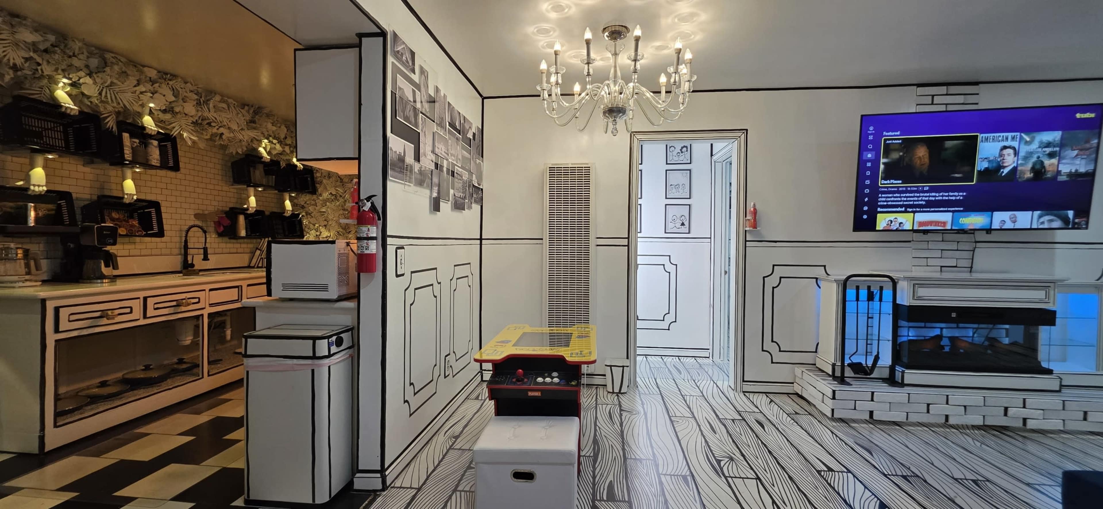 The image shows a modern living space featuring a kitchen area, a stylish chandelier, and a wall-mounted television in a room with a distinctive black and white design.