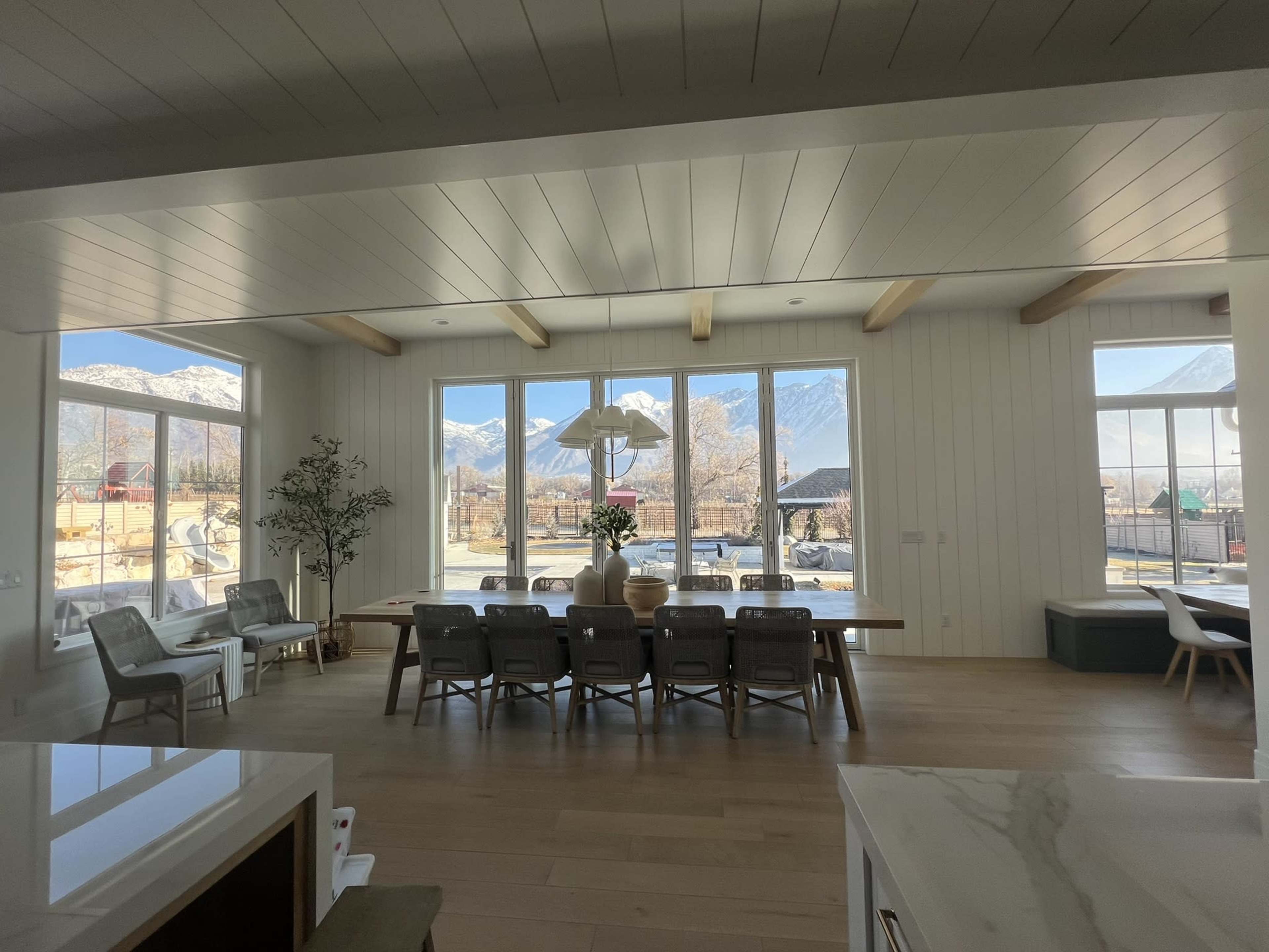 A spacious dining area featuring large windows that showcase mountain views, with a wooden table and gray chairs arranged around it.