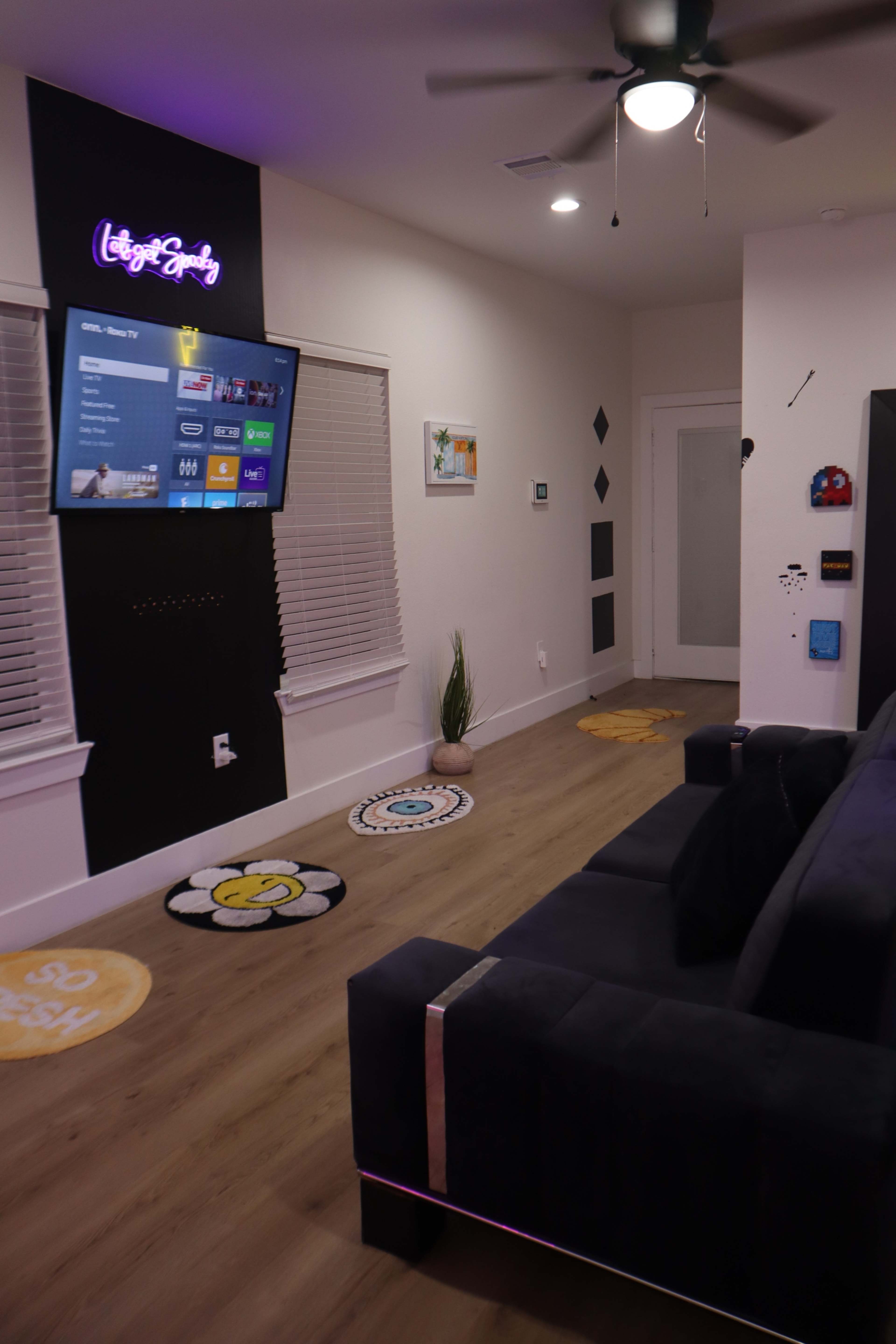 The room features a dark-colored couch facing a wall-mounted television, with decorative rugs and wall art enhancing the modern interior design.