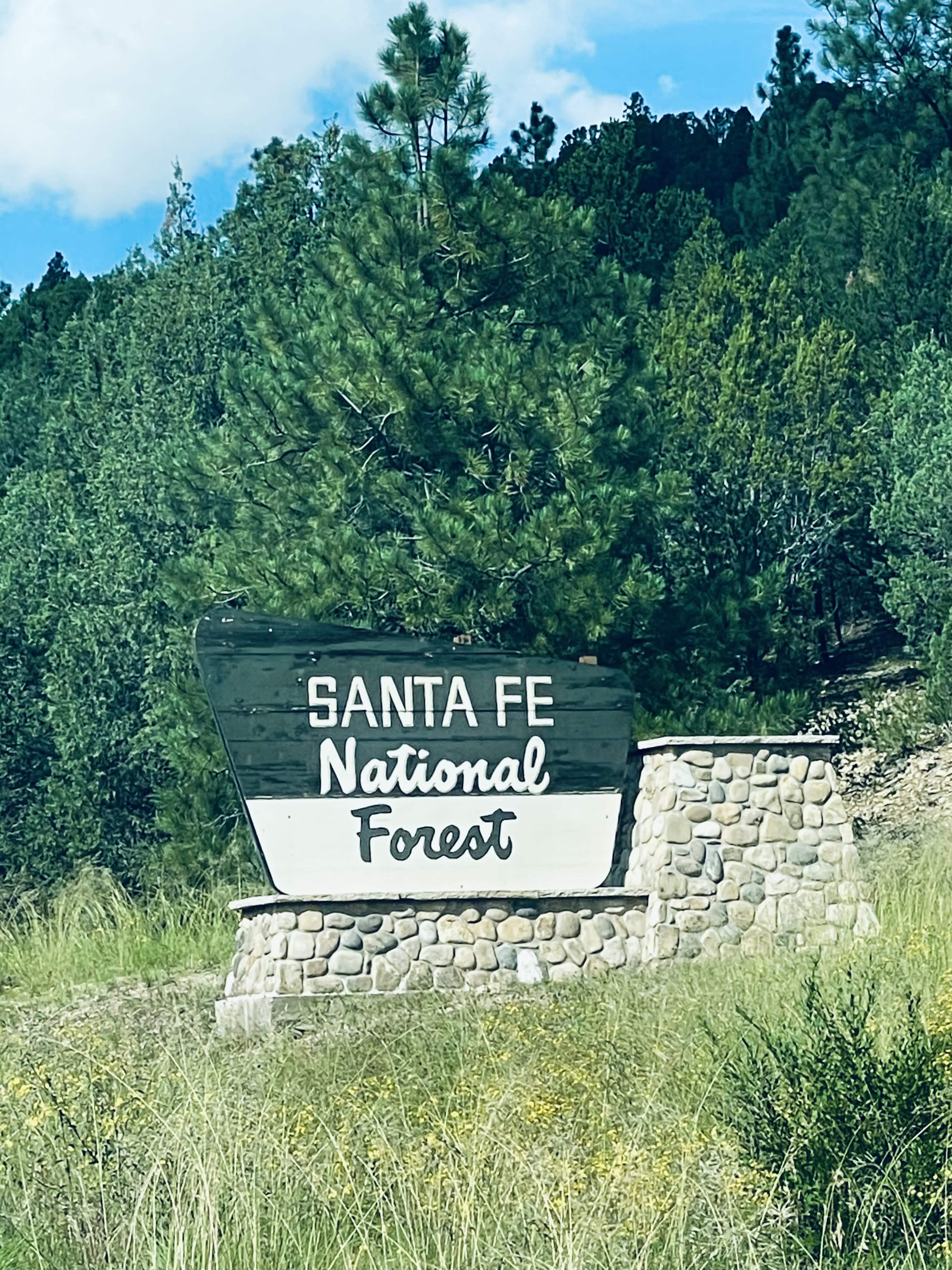 A welcoming sign for Santa Fe National Forest is surrounded by greenery and stone features.