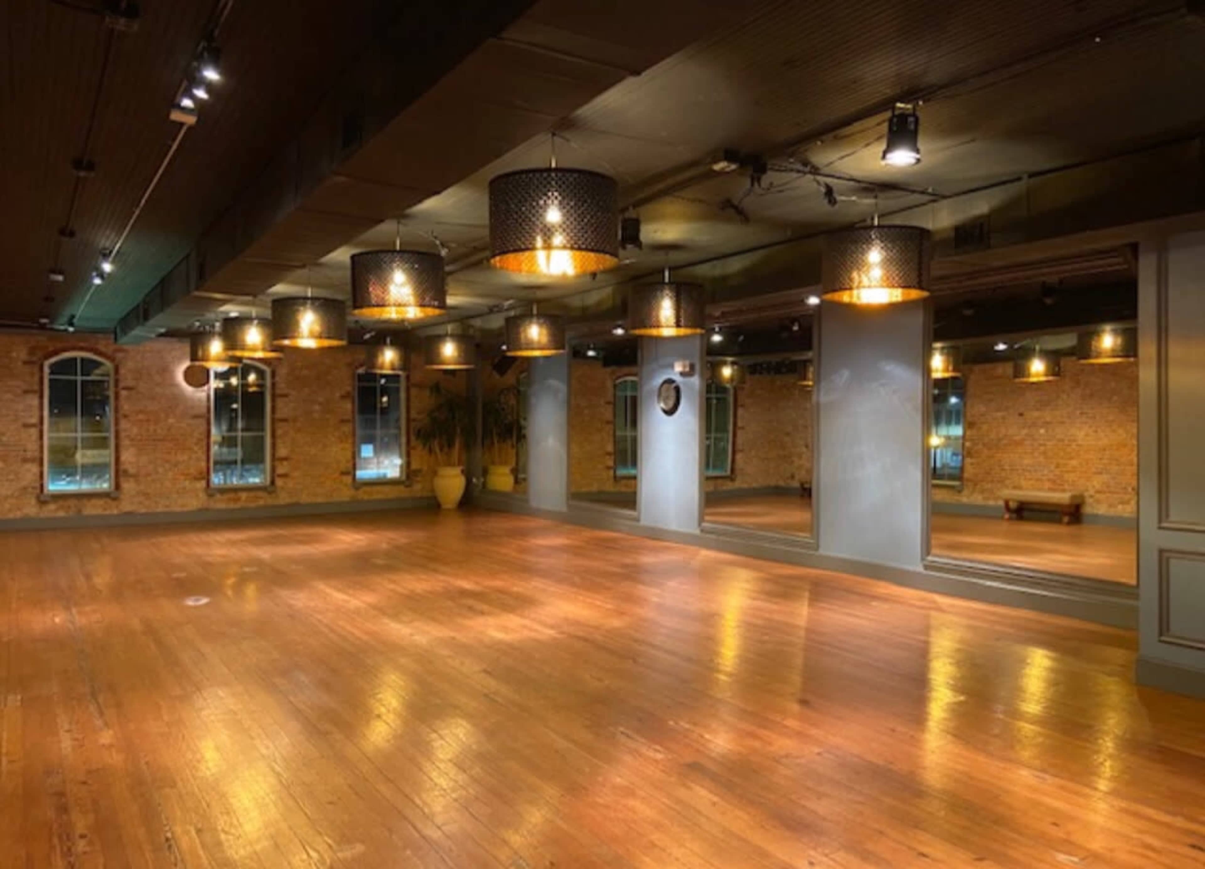 An empty interior space with wooden floors, exposed brick walls, and pendant lighting.