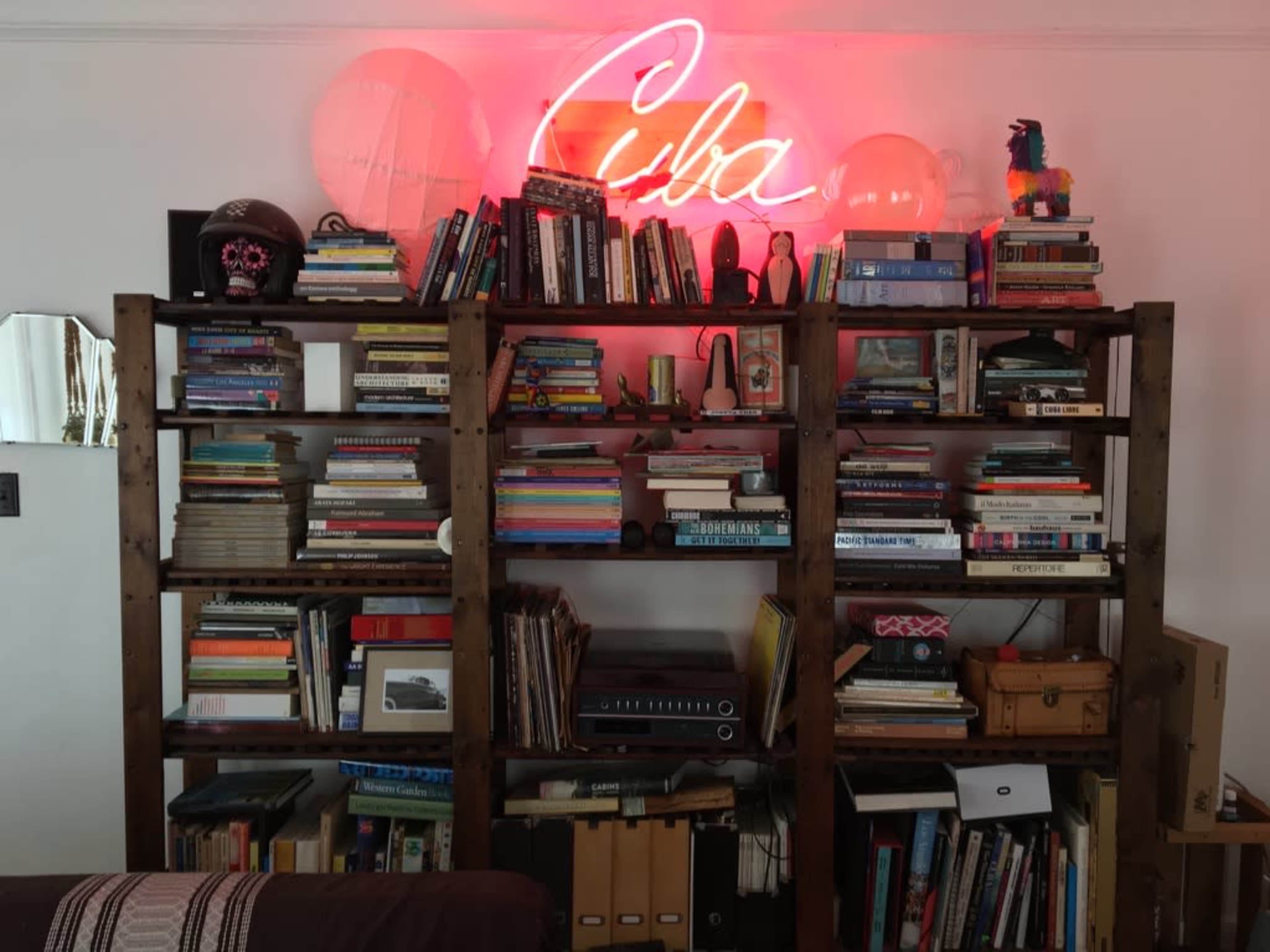 A wooden bookshelf filled with a variety of books, decorative items, and a neon sign that says "Cuba" glowing in red.