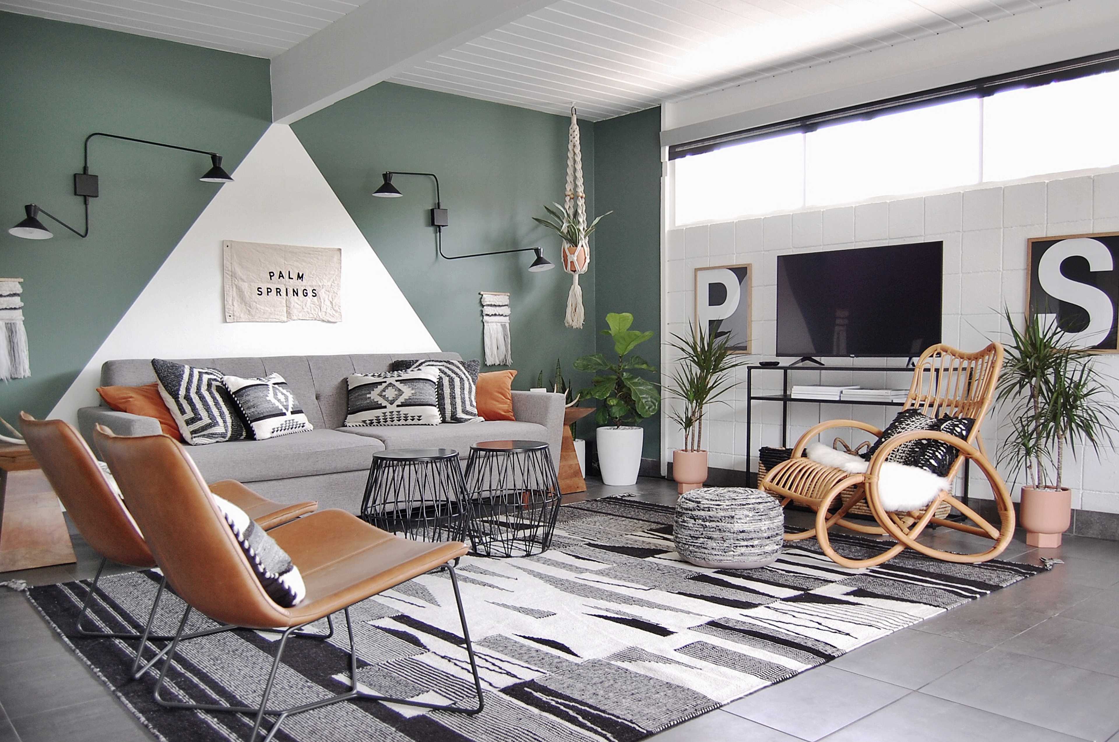 The image shows a modern living room featuring a gray sofa, patterned rug, a television setup, and various decorative plants.