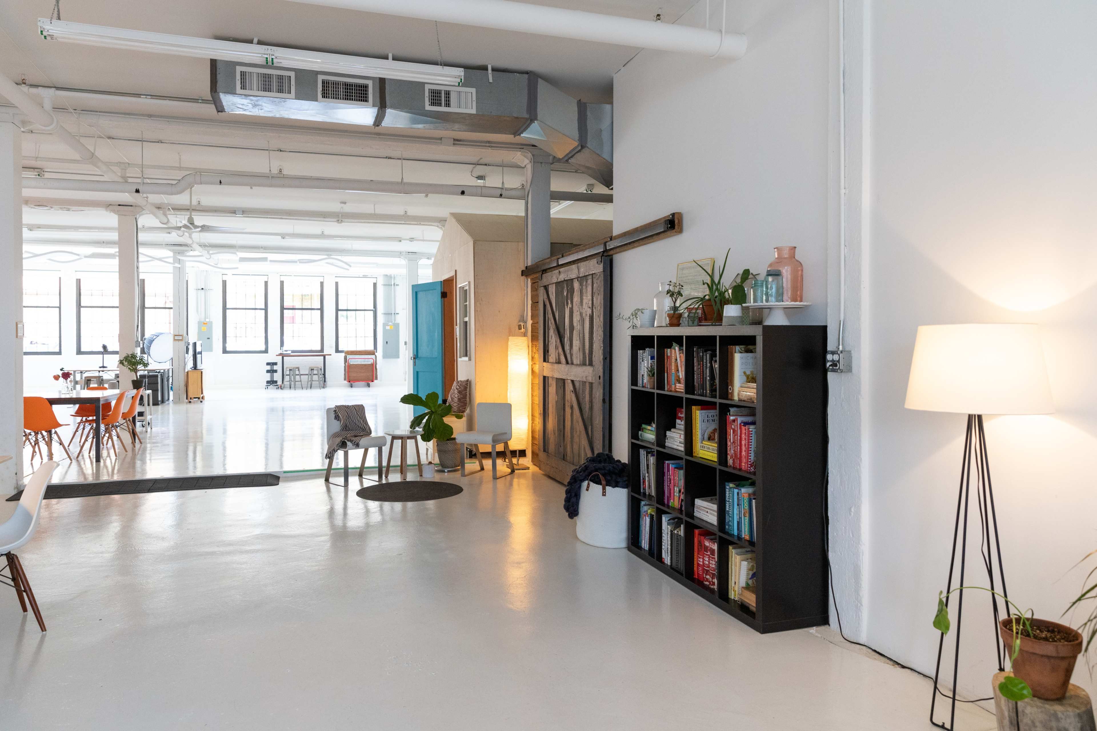 A bright, open workspace with a bookshelf, indoor plants, and various seating arrangements.