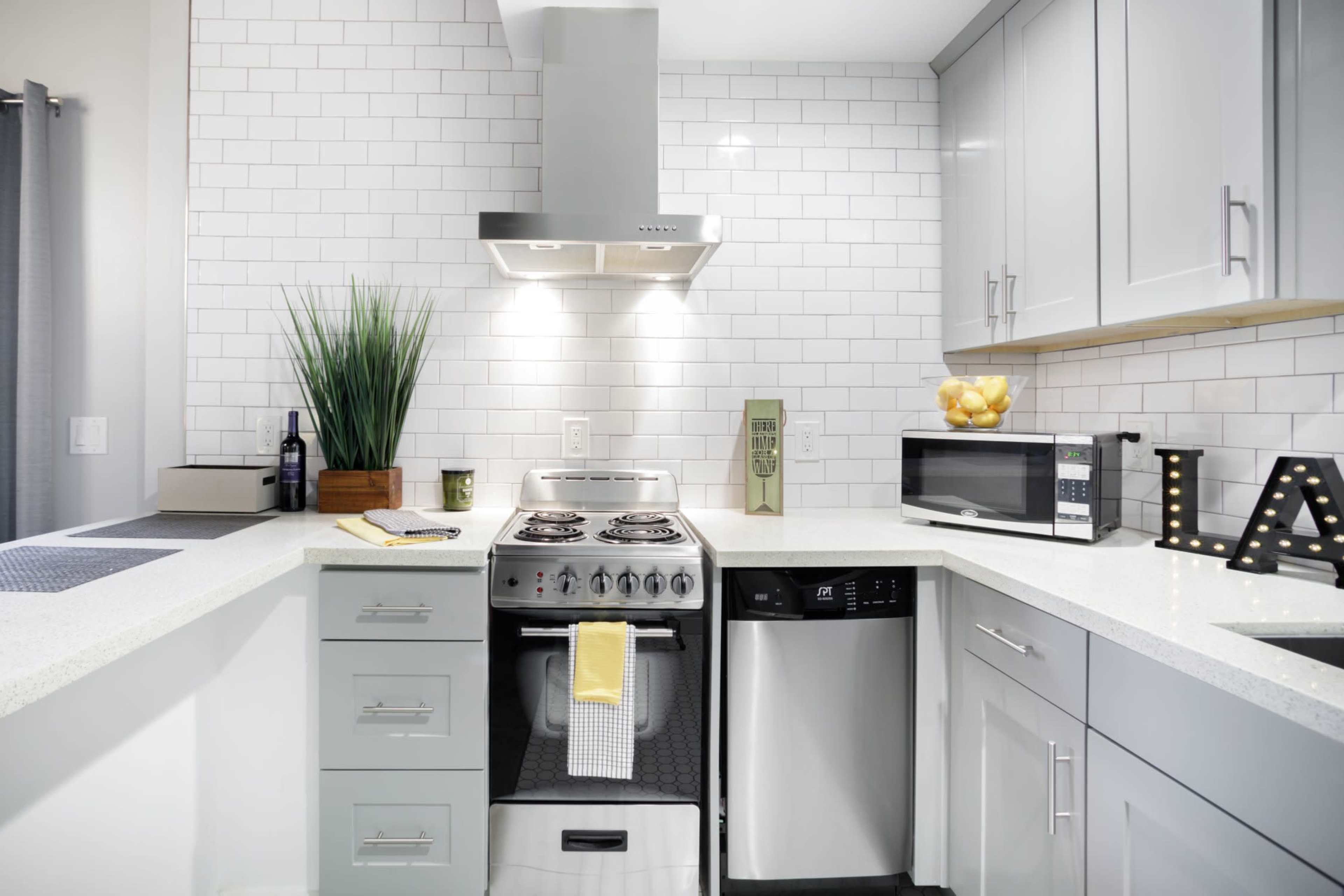 The image shows a modern kitchen with gray cabinetry, a white countertop, and stainless steel appliances, including a stove, microwave, and dishwasher.