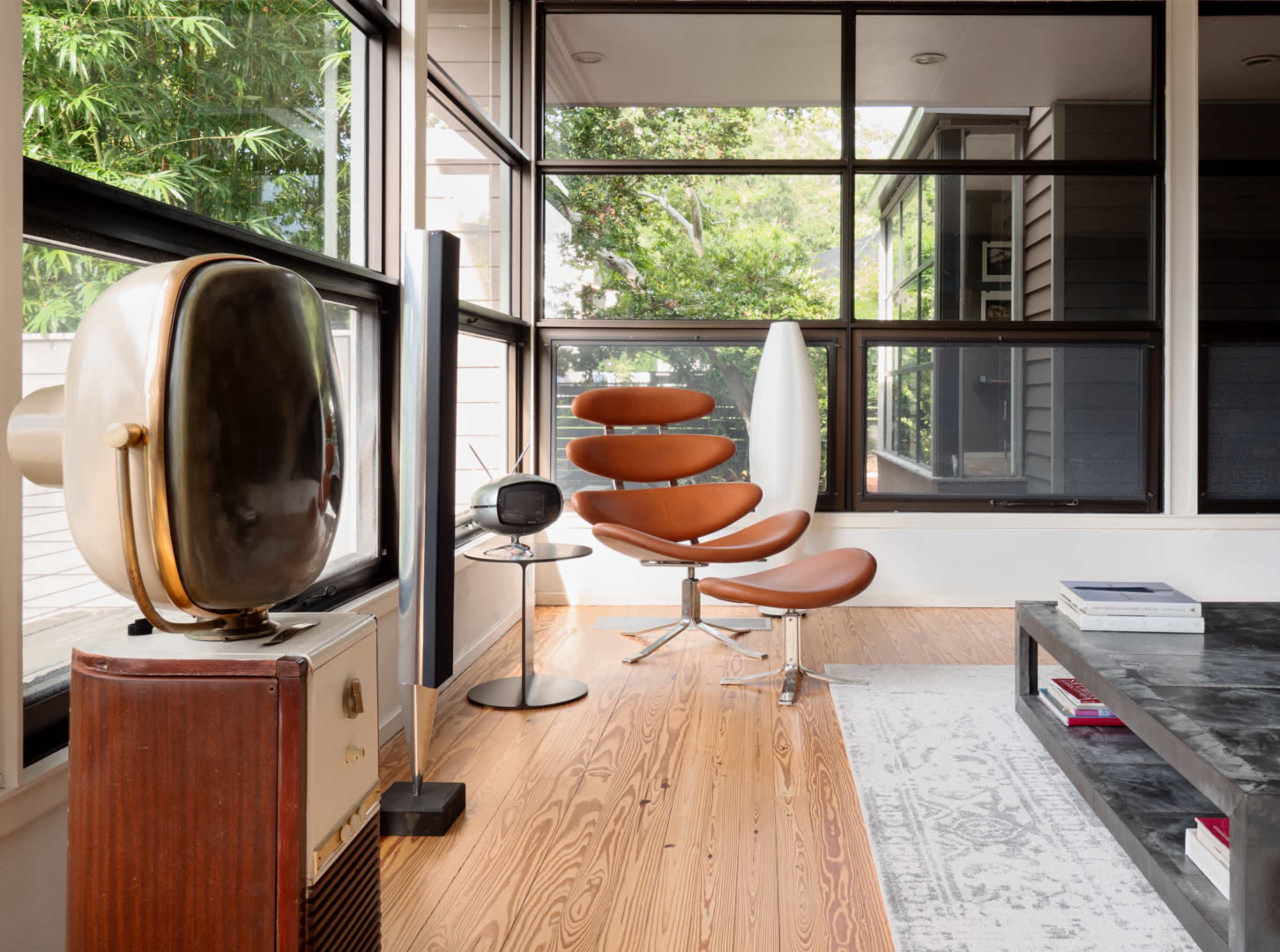 A modern interior with large windows, featuring a brown lounge chair, a sleek standing lamp, and a vintage television set on a table.