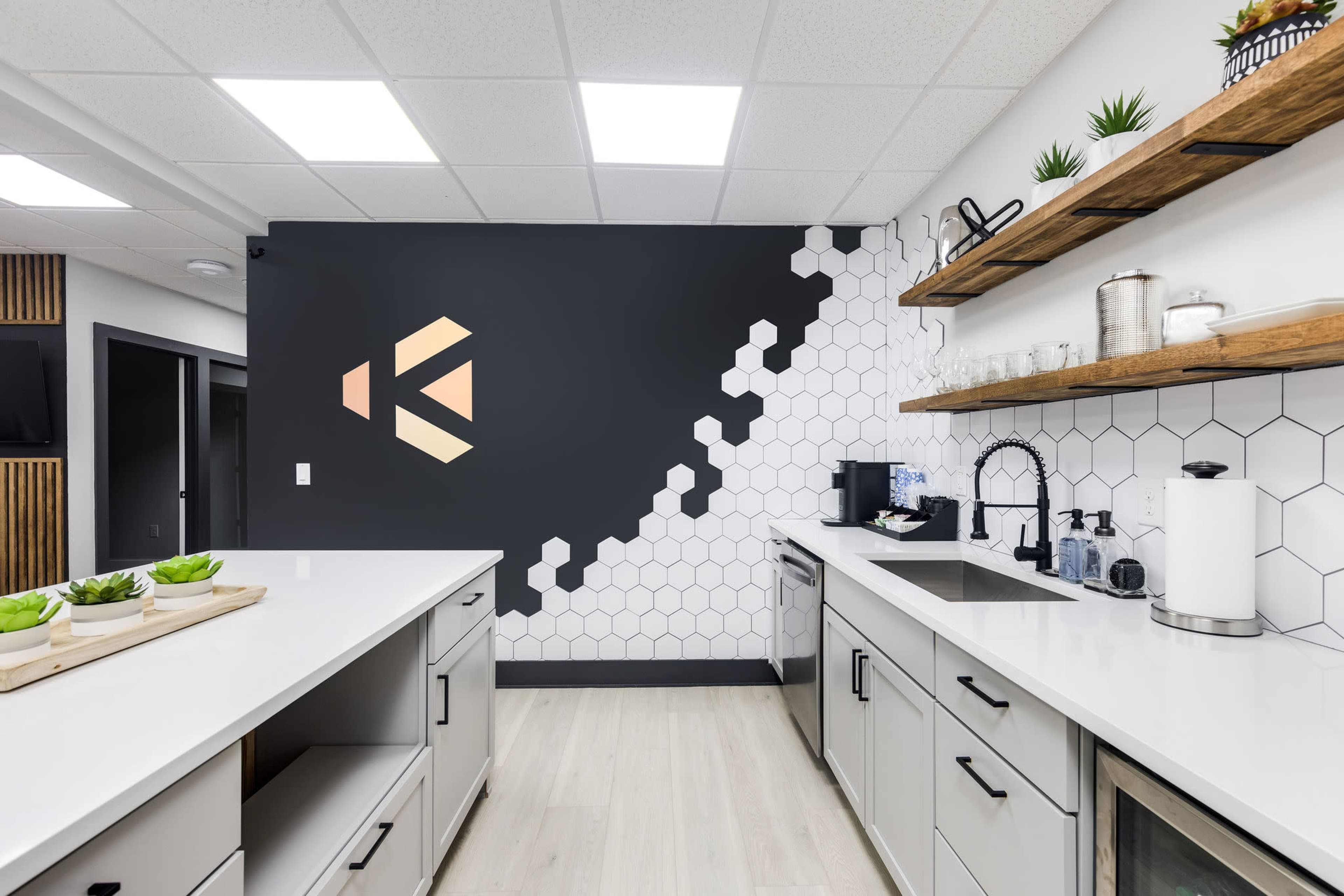 A modern kitchen space with hexagonal tile, wooden shelving, and a black accent wall featuring a geometric design.