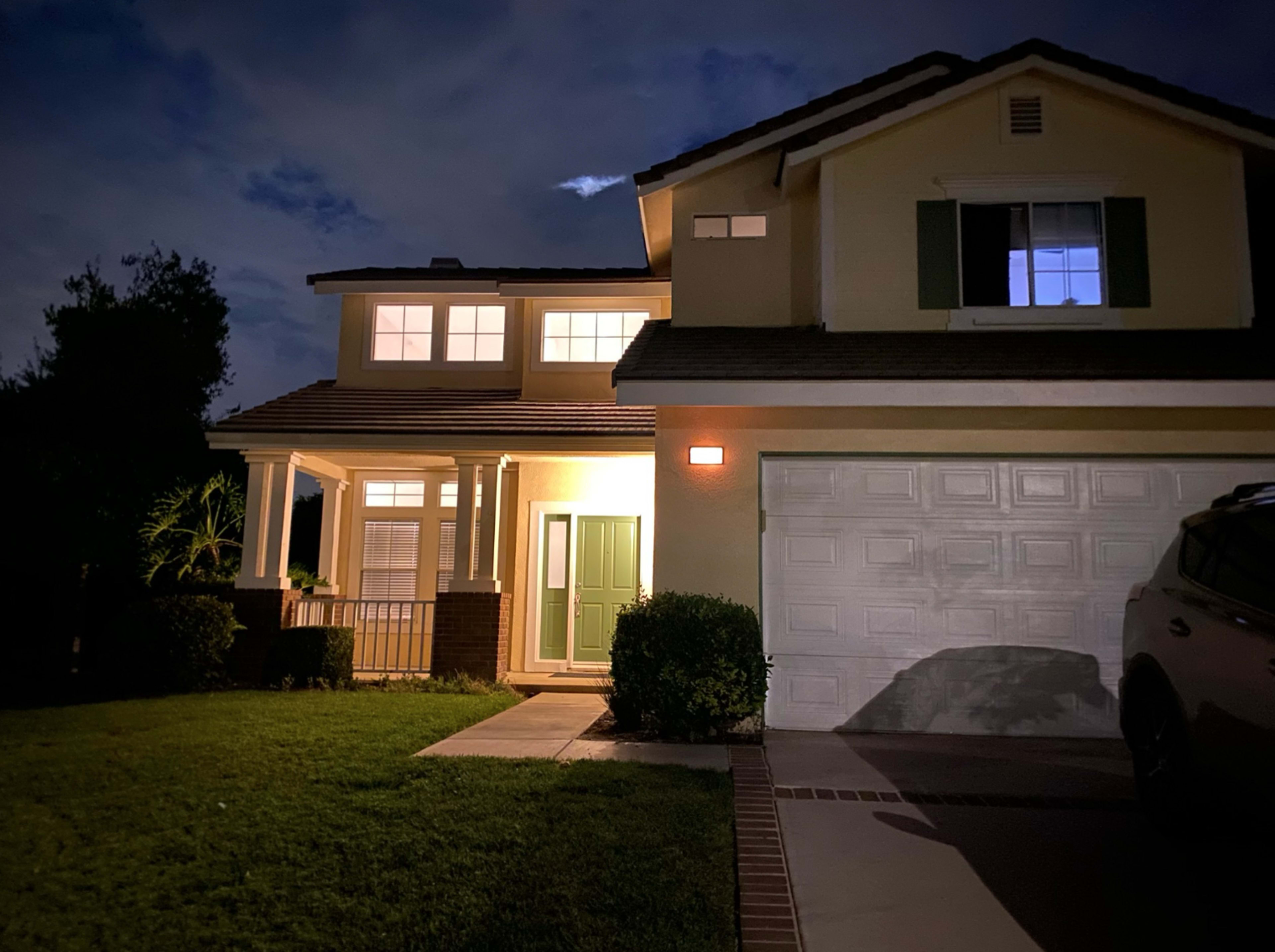 A two-story house is illuminated at night, with a front porch and a car parked in the driveway.