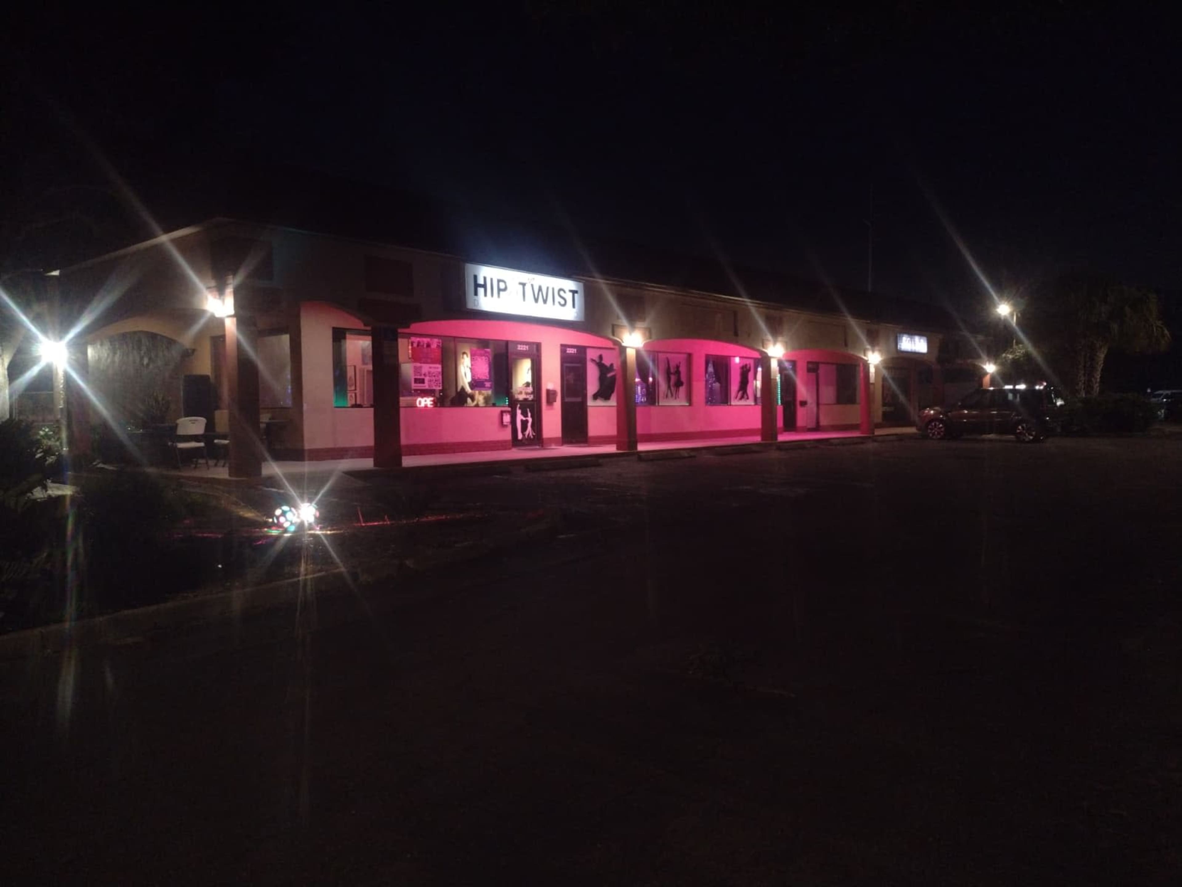 The exterior of a building named "HIP TWIST" is illuminated at night with pink lights, showcasing large window displays.