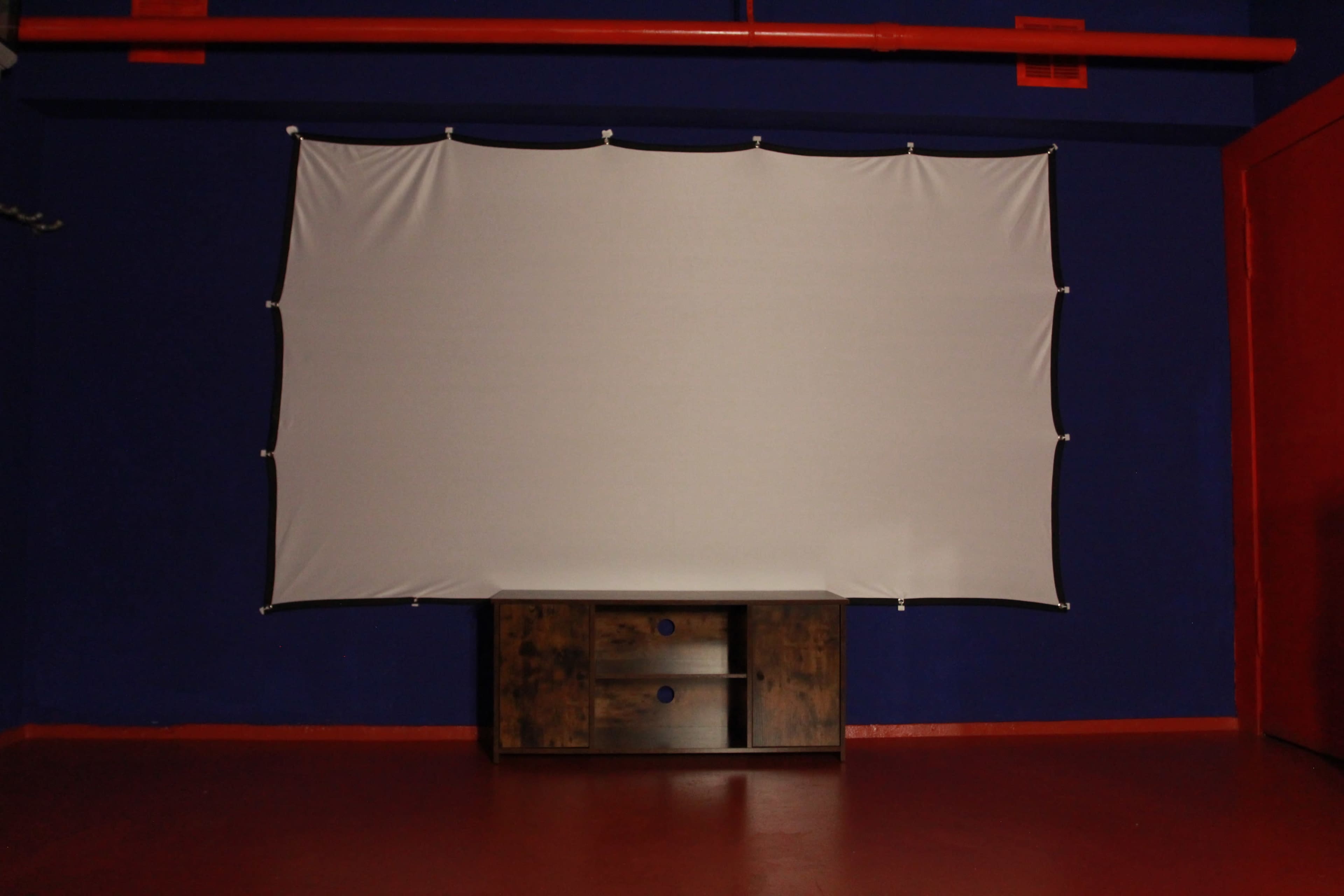 A white screen is suspended on a blue wall above a wooden cabinet in a red-painted room.