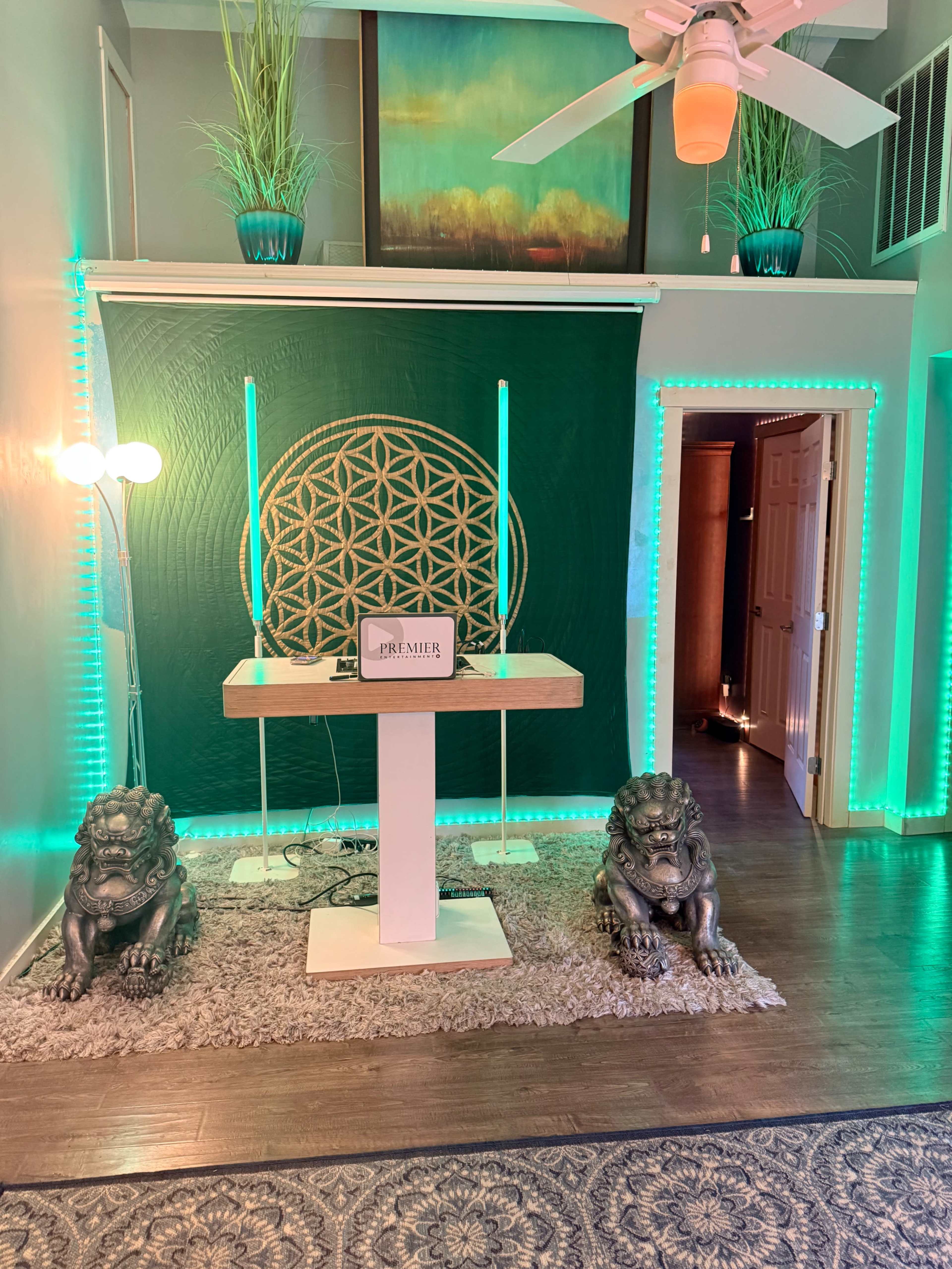 The image depicts a room with a decorative backdrop featuring a large geometric design, flanked by two lion statues and illuminated by green LED lights.