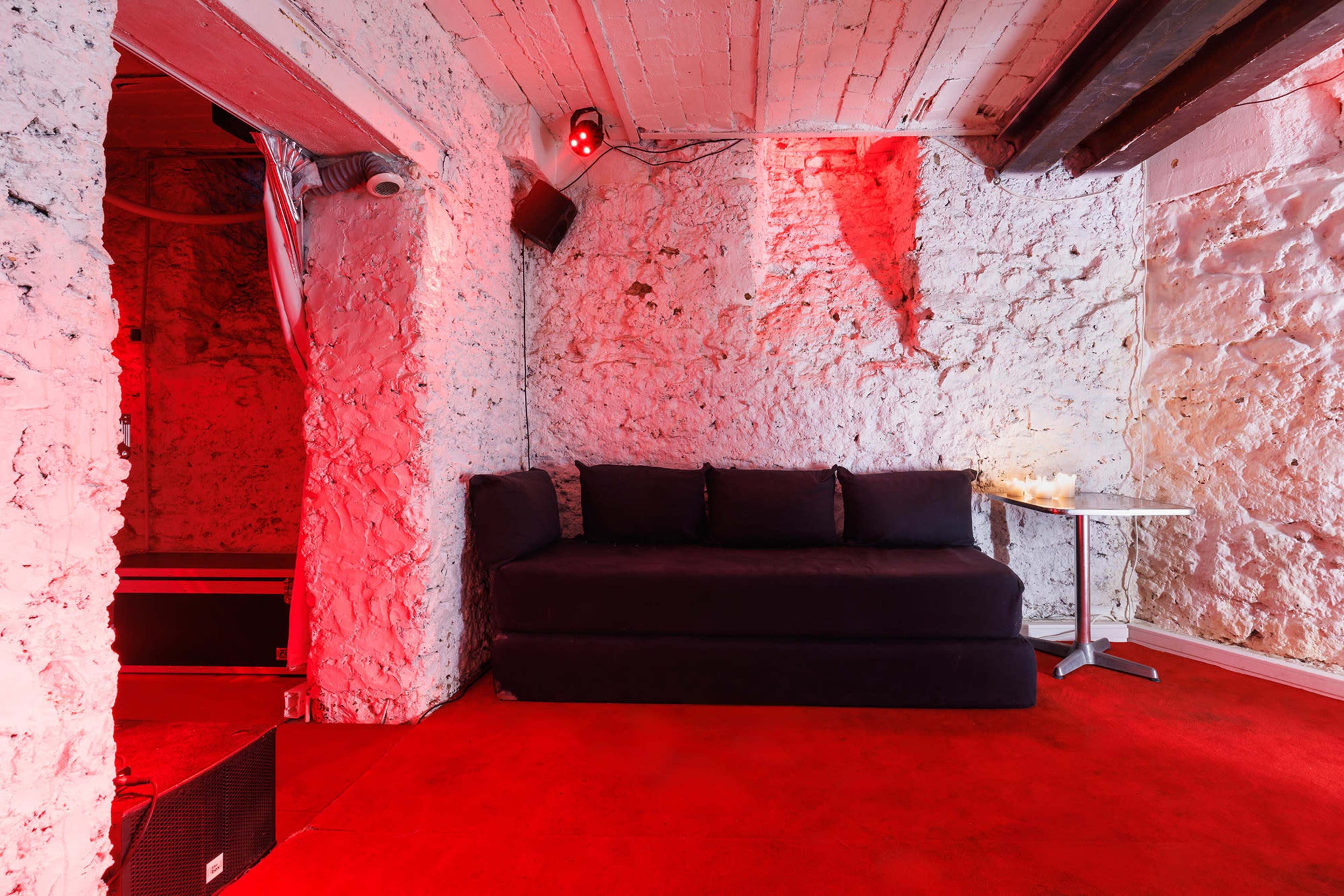 The image shows a dimly lit room with stone walls, red lighting, a dark sofa, and a small table.