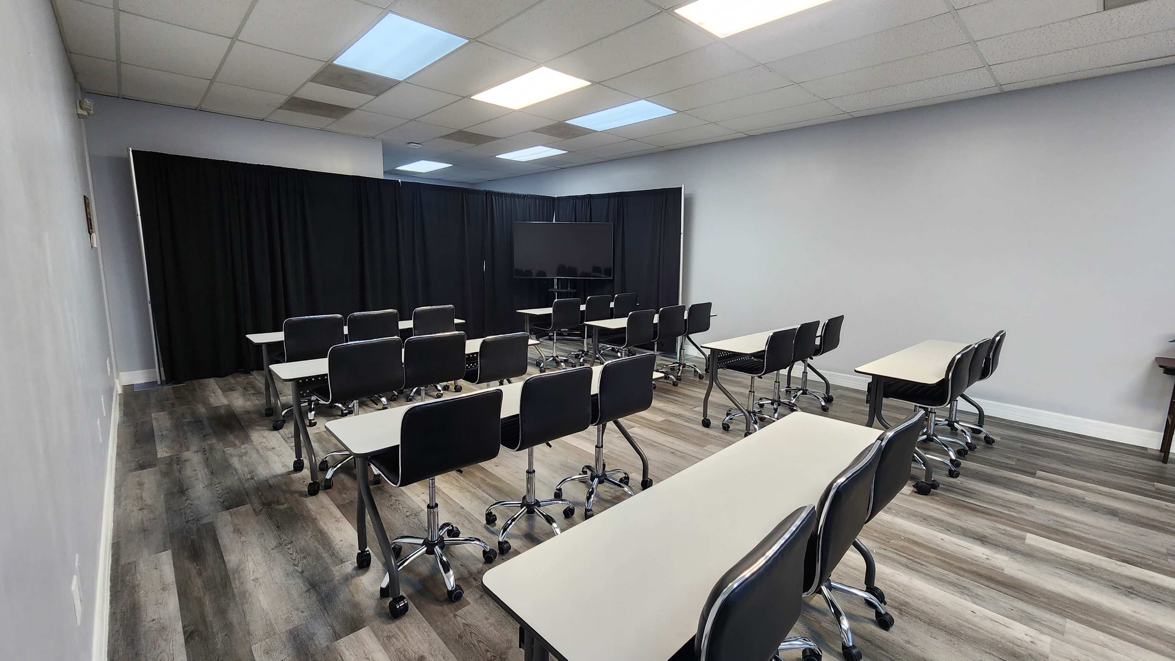 A classroom with rows of desks and chairs arranged facing a large screen, separated by black curtains at the back.