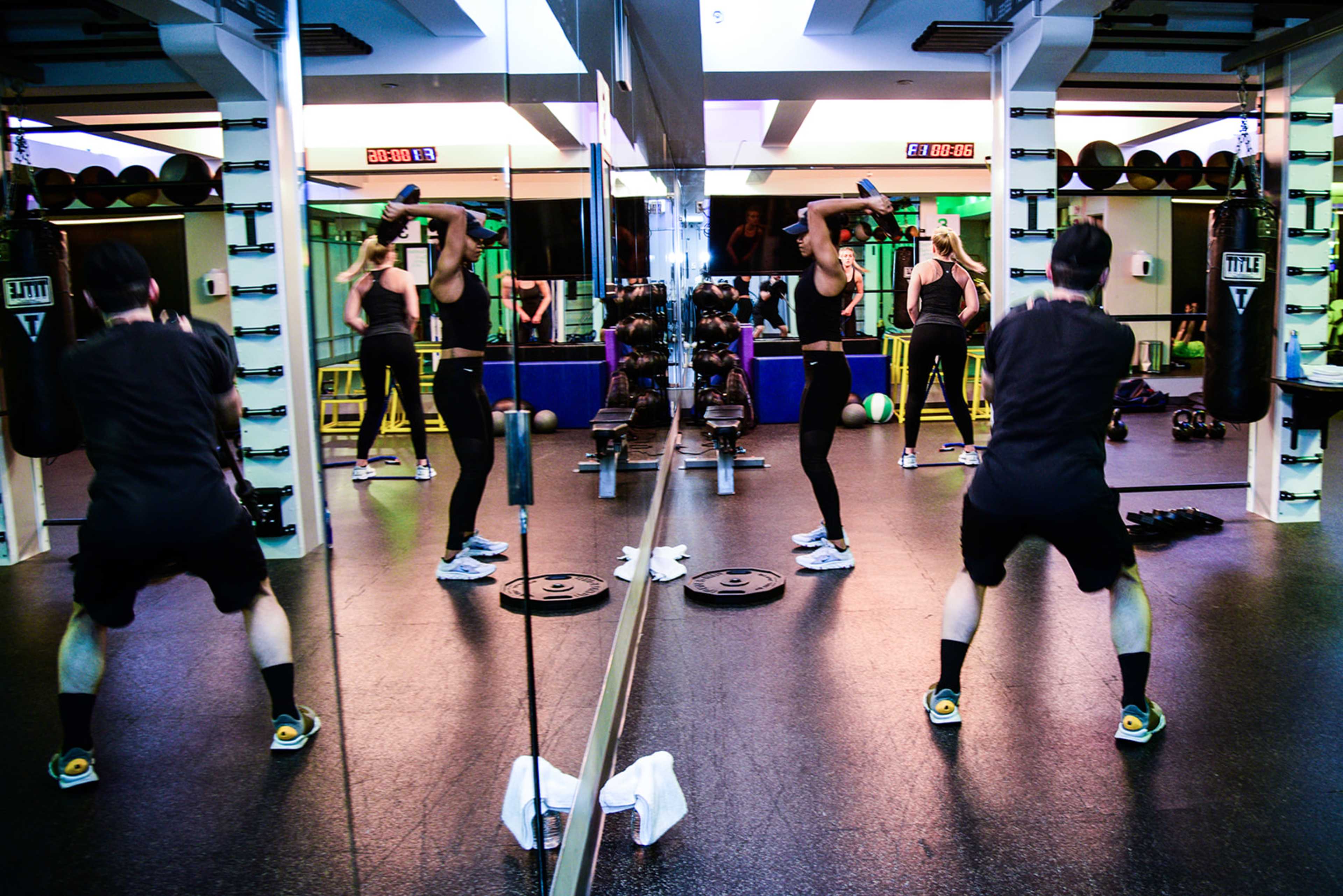 A gym scene shows individuals engaged in weightlifting exercises in front of a mirrored wall.