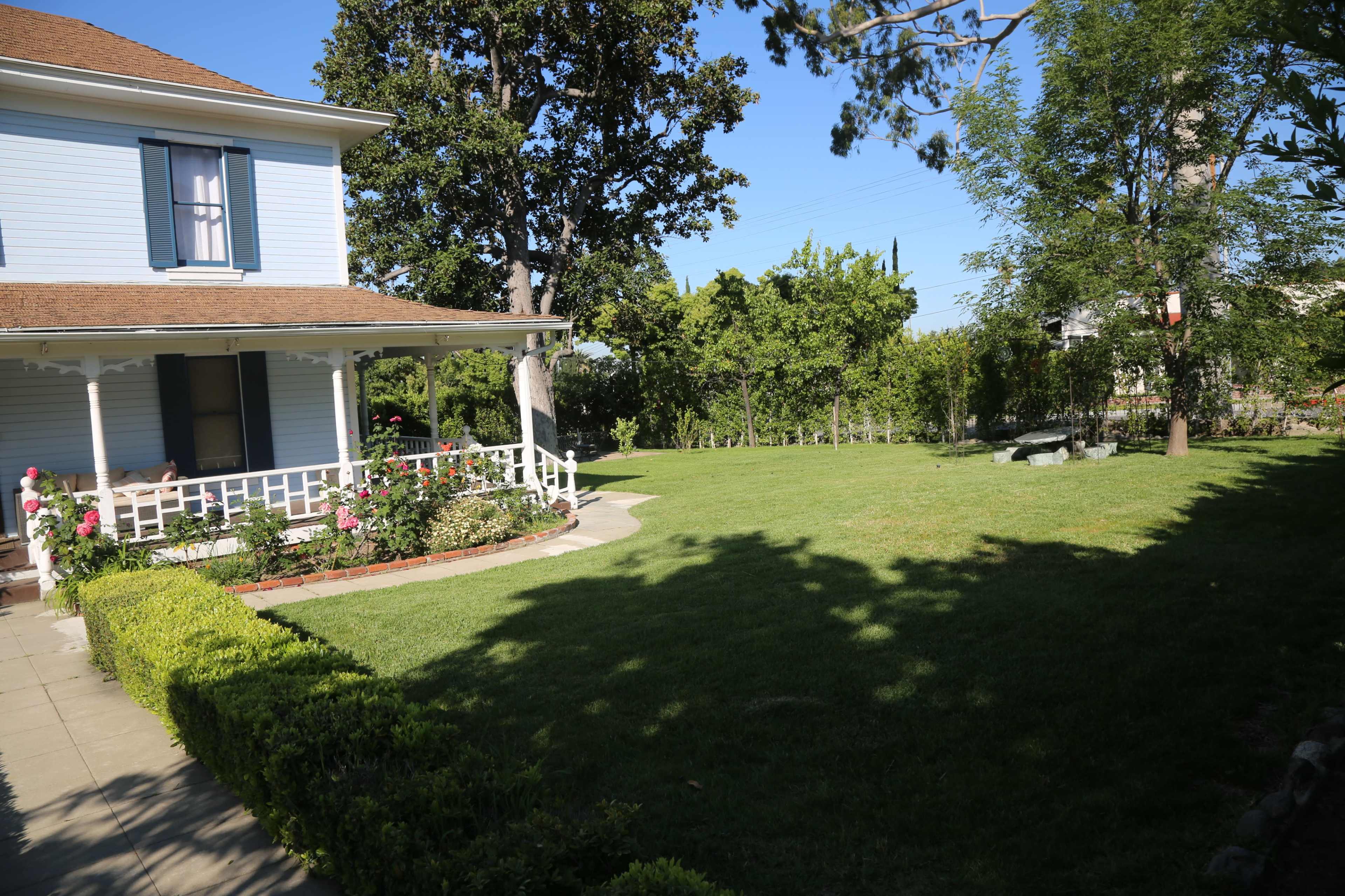A well-maintained lawn surrounds a two-story blue house with a porch and landscaped garden.