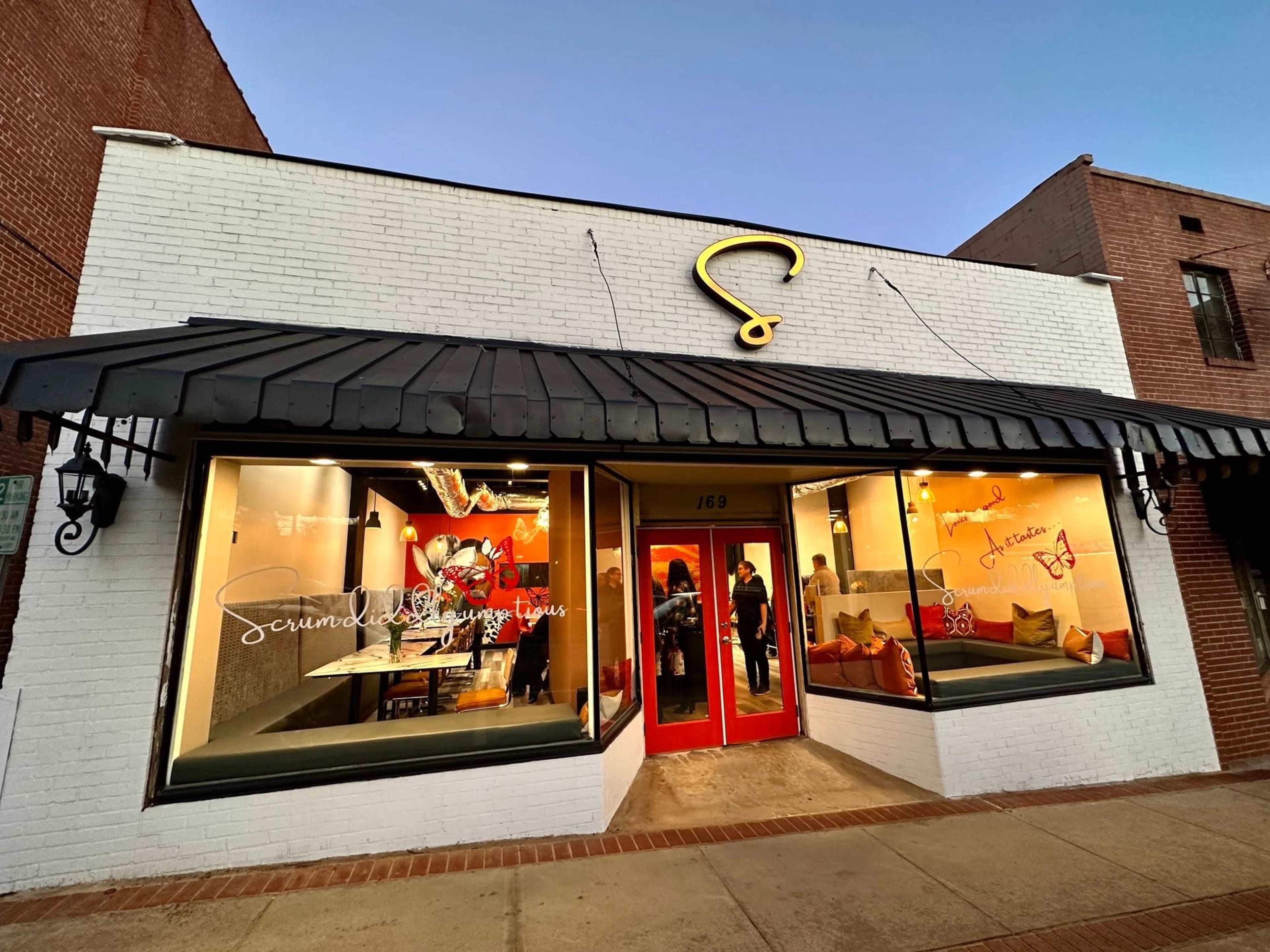 A brightly lit bakery storefront with large windows, featuring a red door and a distinctive yellow sign above.