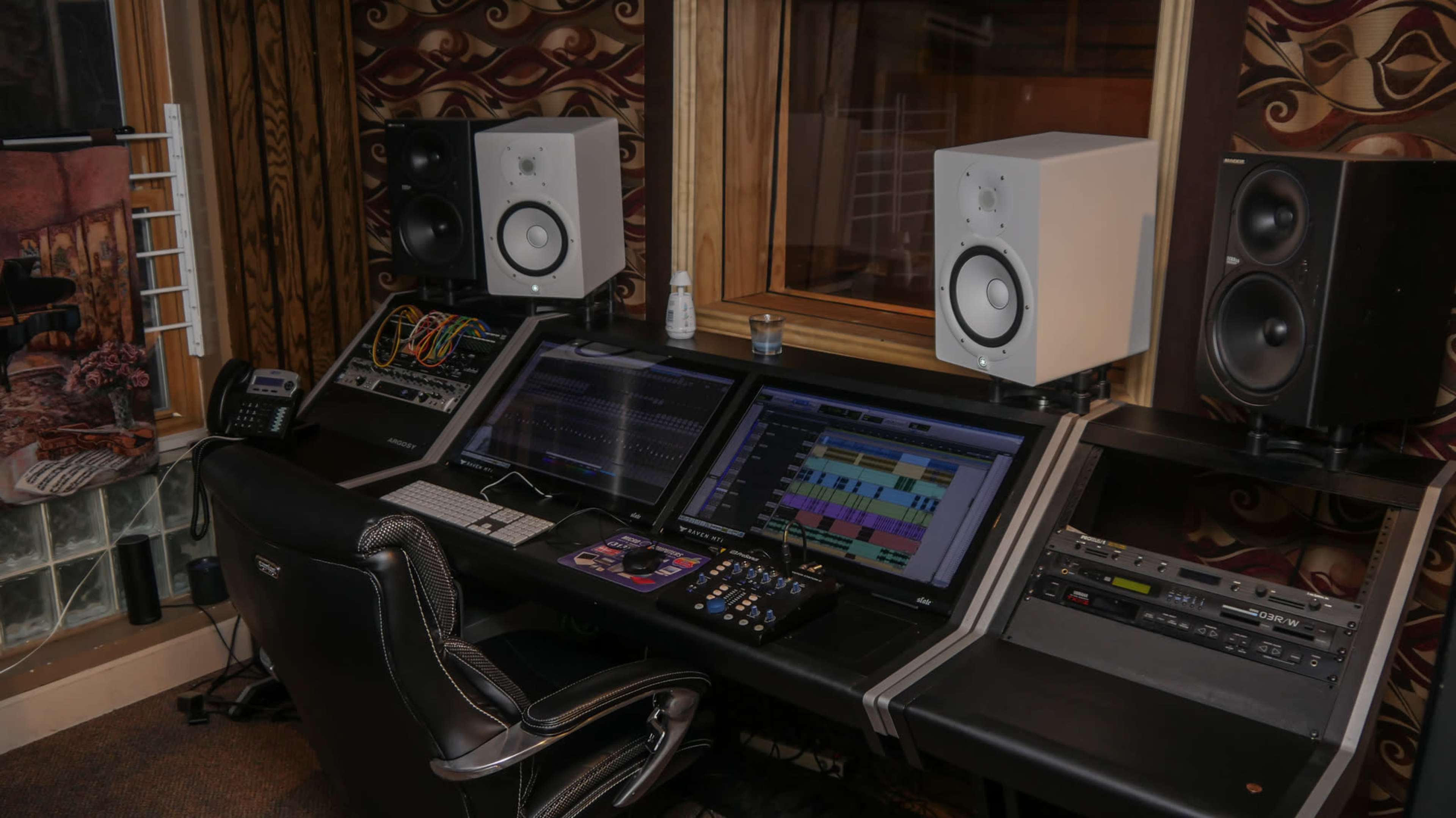 A sound mixing studio featuring dual computer monitors, studio monitors, and various audio equipment arranged on a sleek desk.