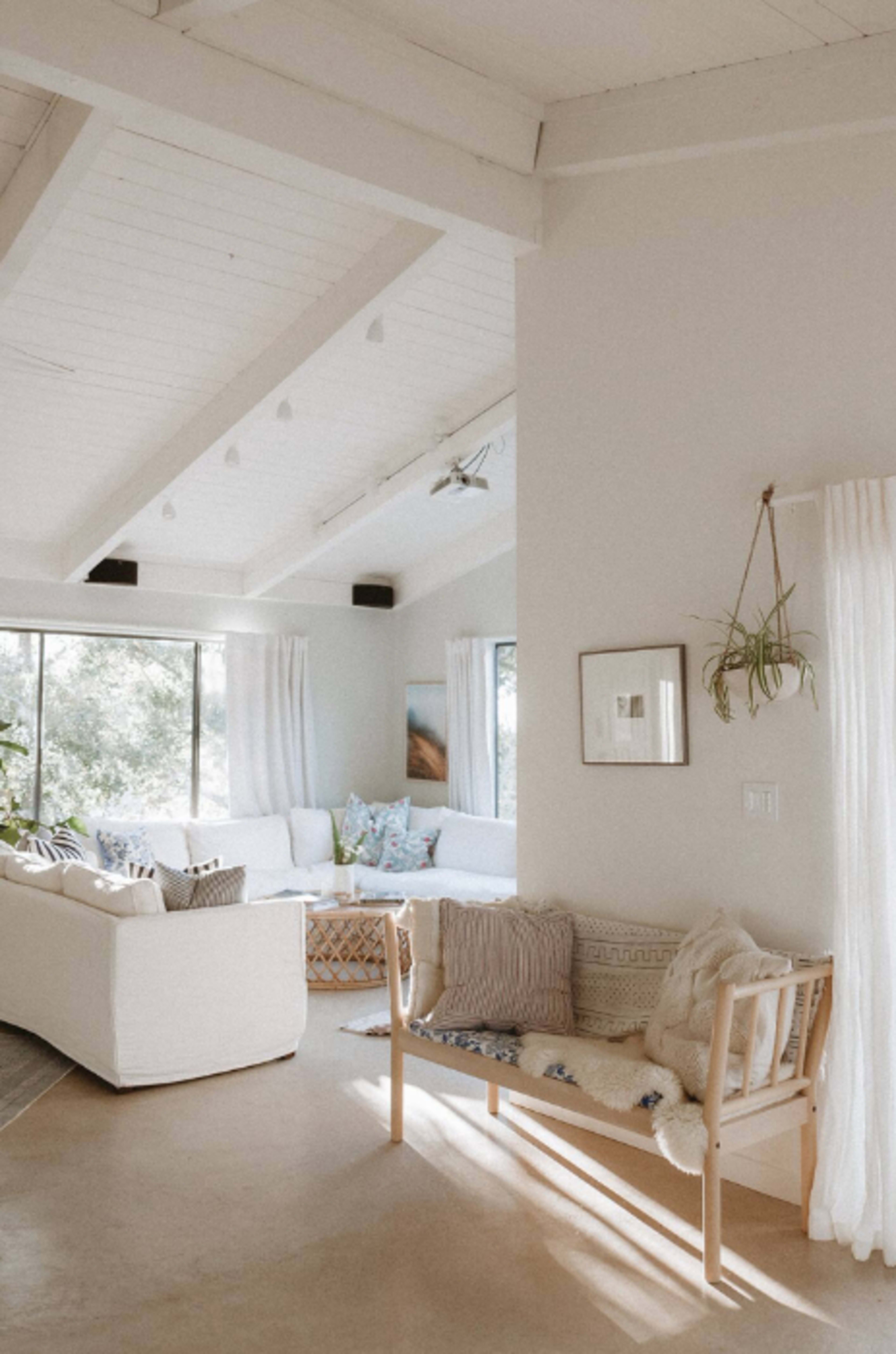 A bright living room features a white sofa, a wooden bench, and large windows allowing natural light to fill the space.