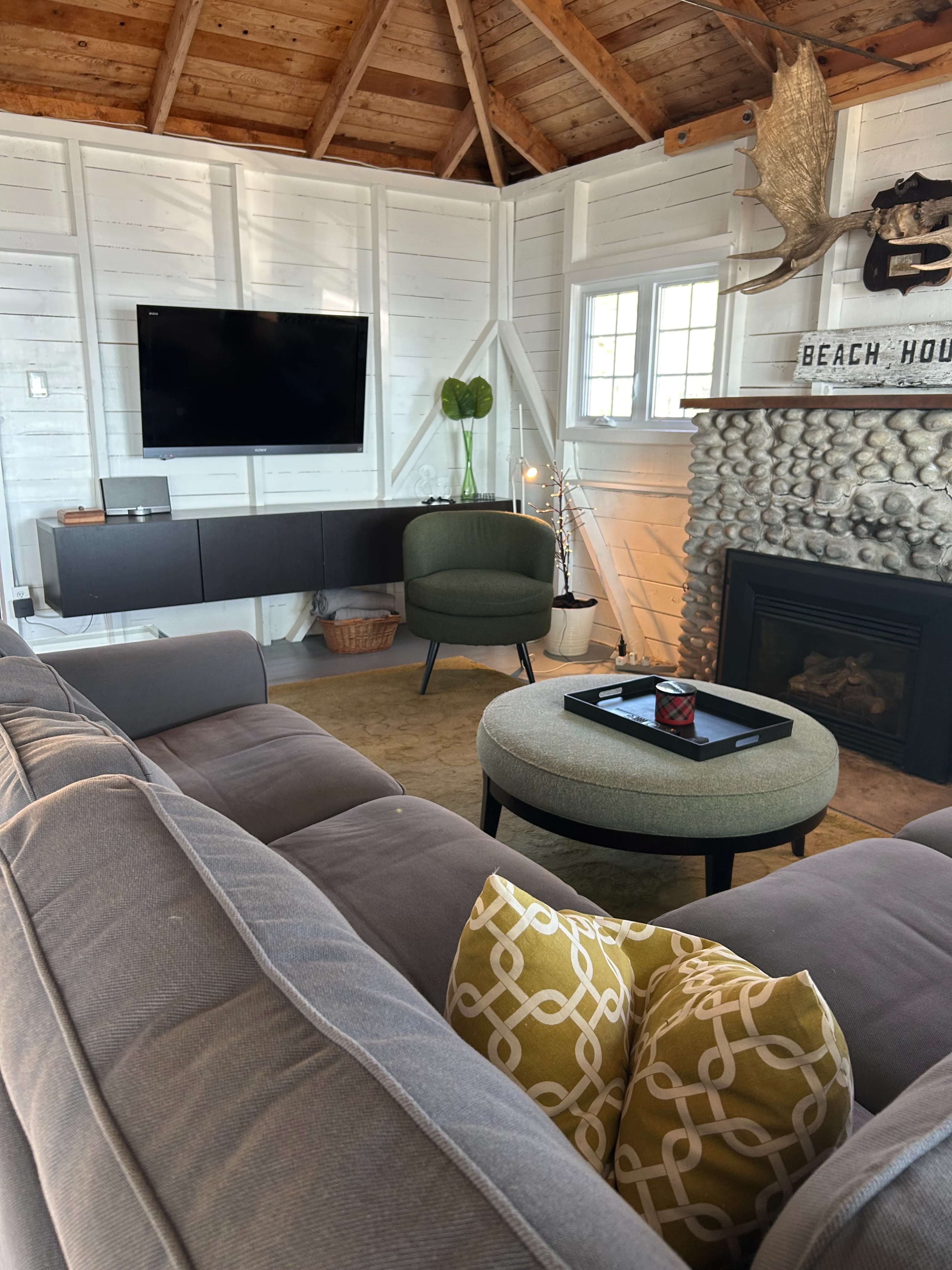 The scene shows a cozy living area with a television mounted on a white wall, a green accent chair, and a round coffee table atop a beige rug.