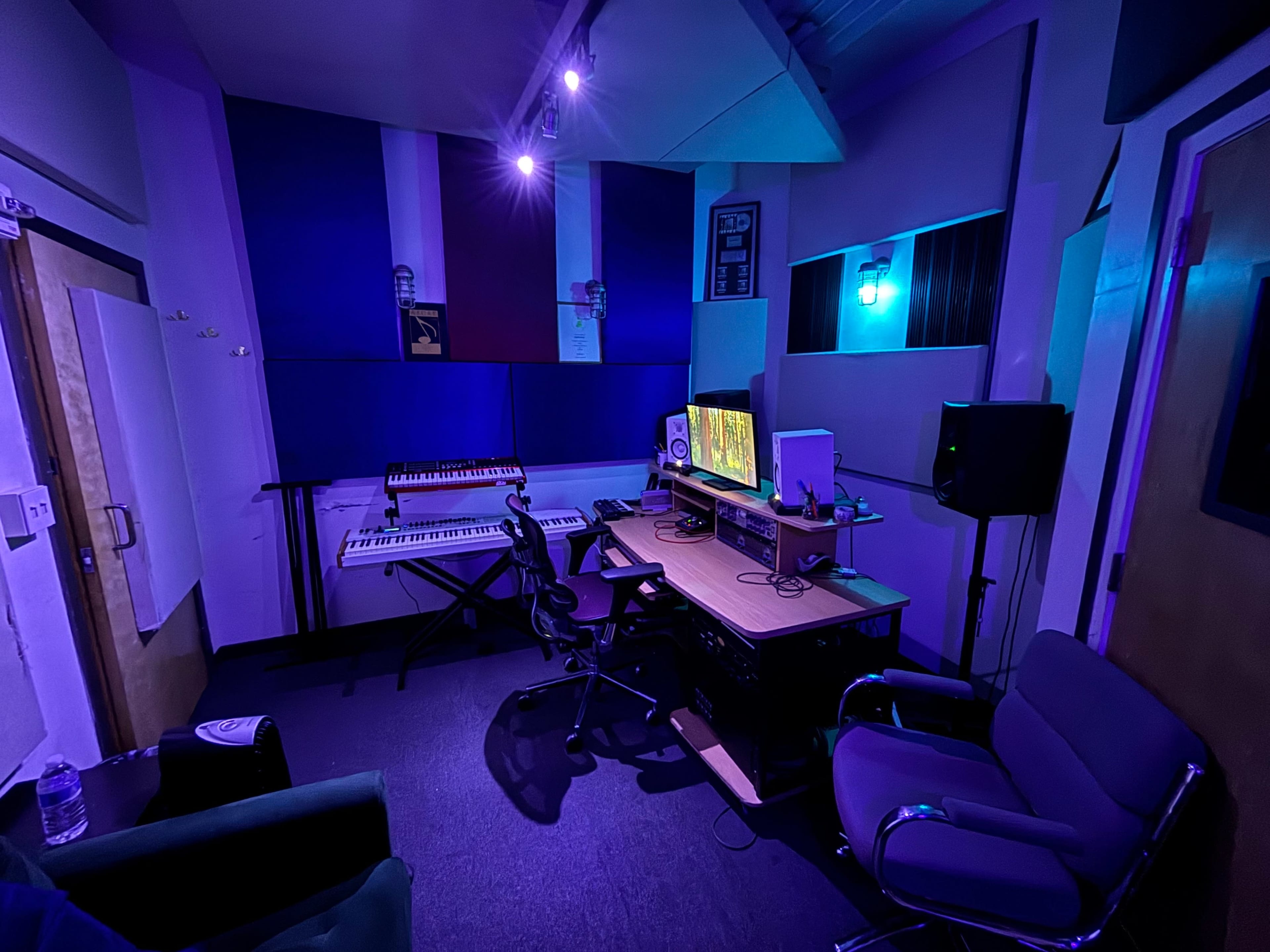 The image shows a music studio with a computer desk, keyboard, and sound equipment, surrounded by purple and blue lighting.