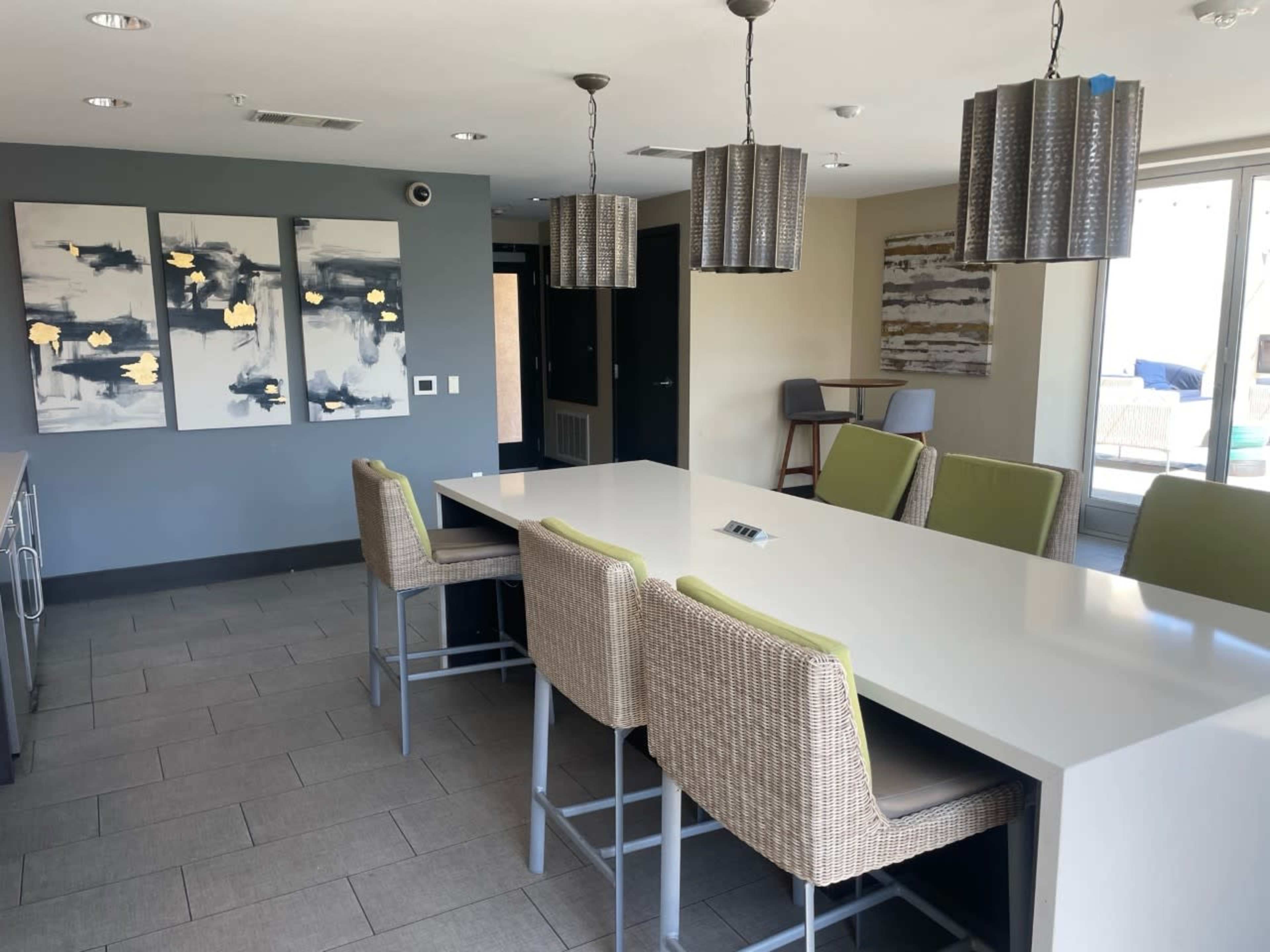 A modern kitchen and dining area featuring a long white table with high stools, pendant lighting, and abstract art on the walls.