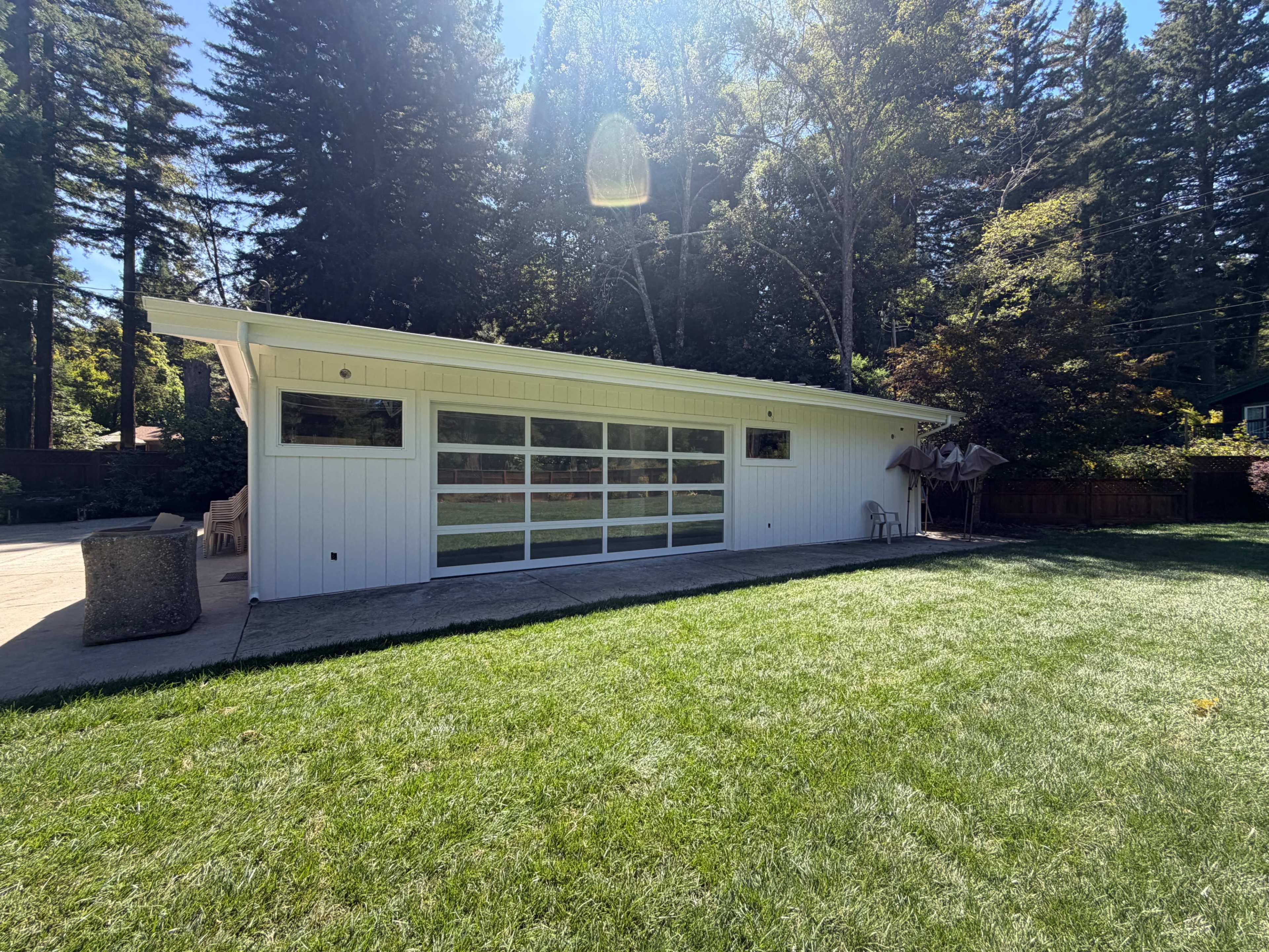 A modern white building with large glass garage doors sits on a grassy lawn surrounded by trees.