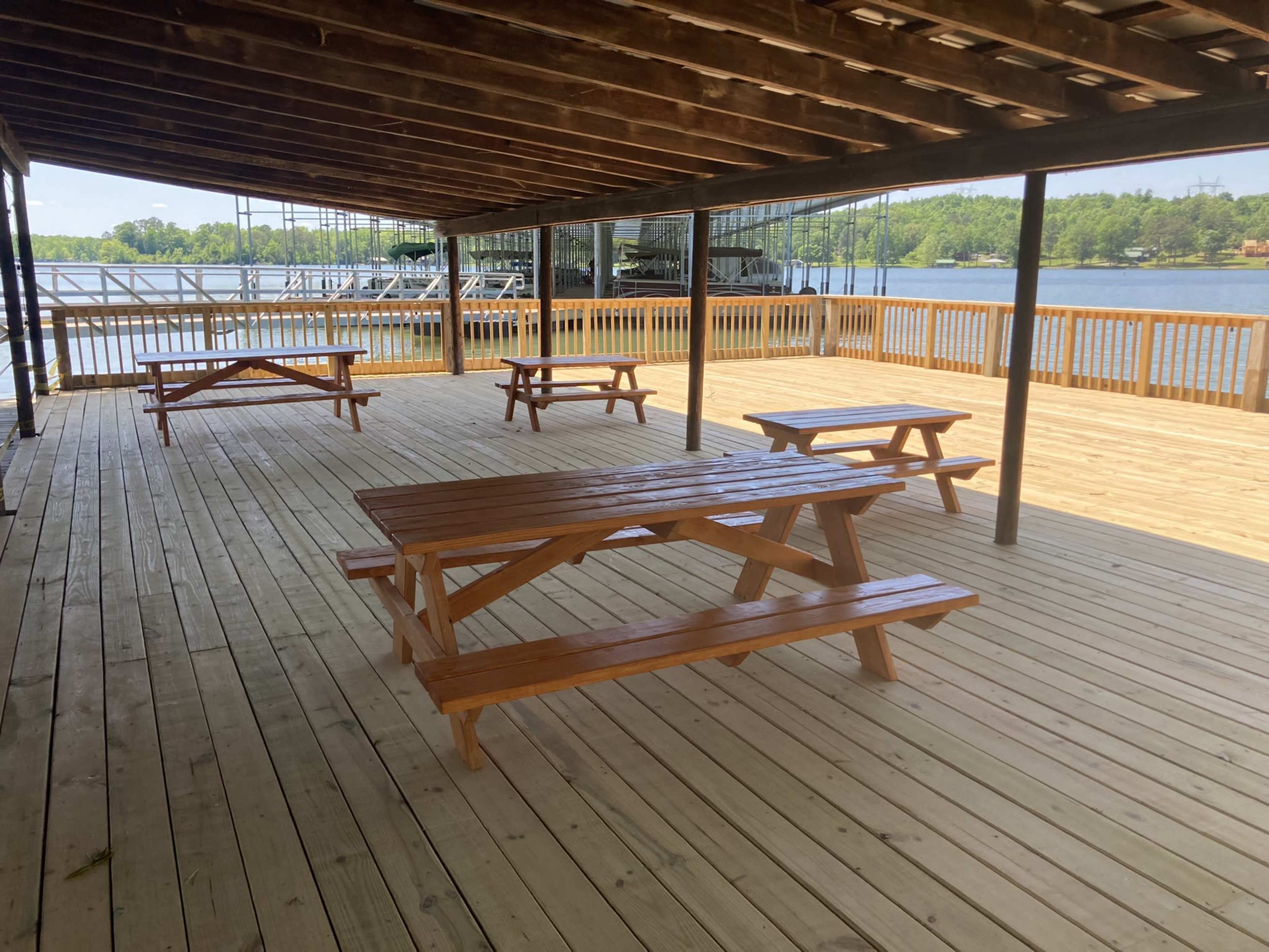 A spacious wooden deck with several picnic tables overlooking a body of water, surrounded by trees.