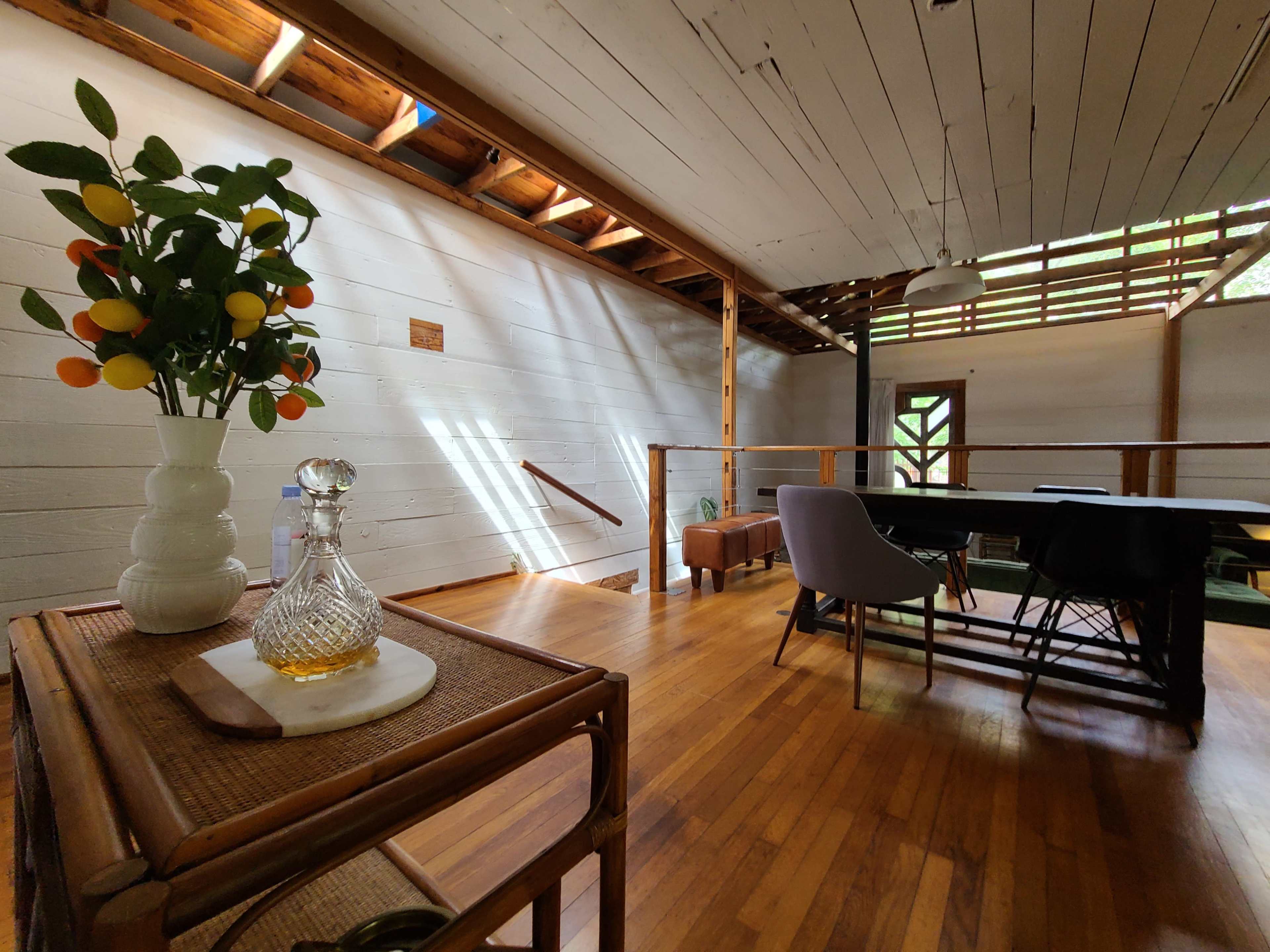 A modern interior space with wooden floors, a dining table, a staircase, and a decorative vase with fruit on a side table.