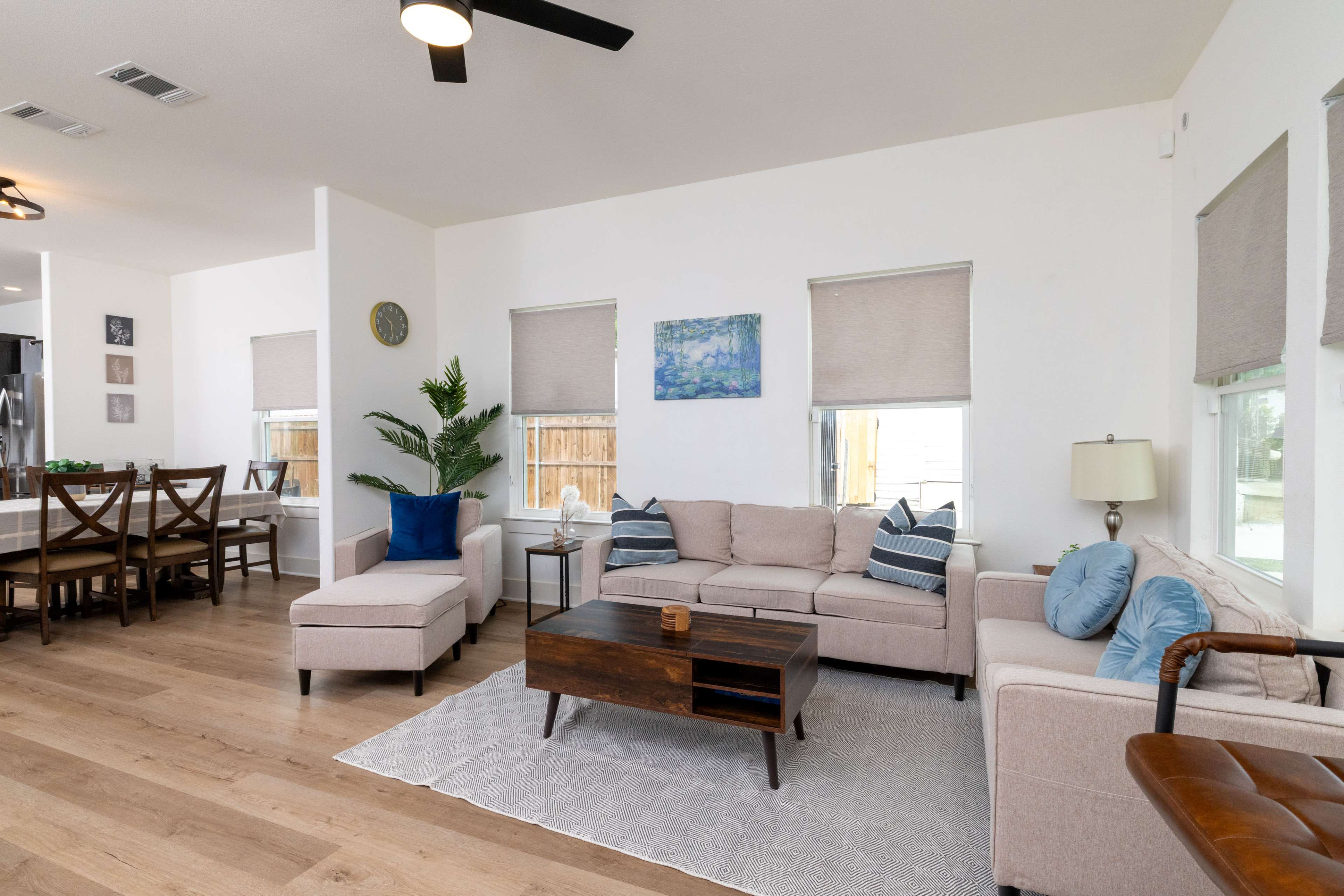 The scene features a modern living room with a light-colored sectional sofa, a wooden coffee table, and a dining area in the background.
