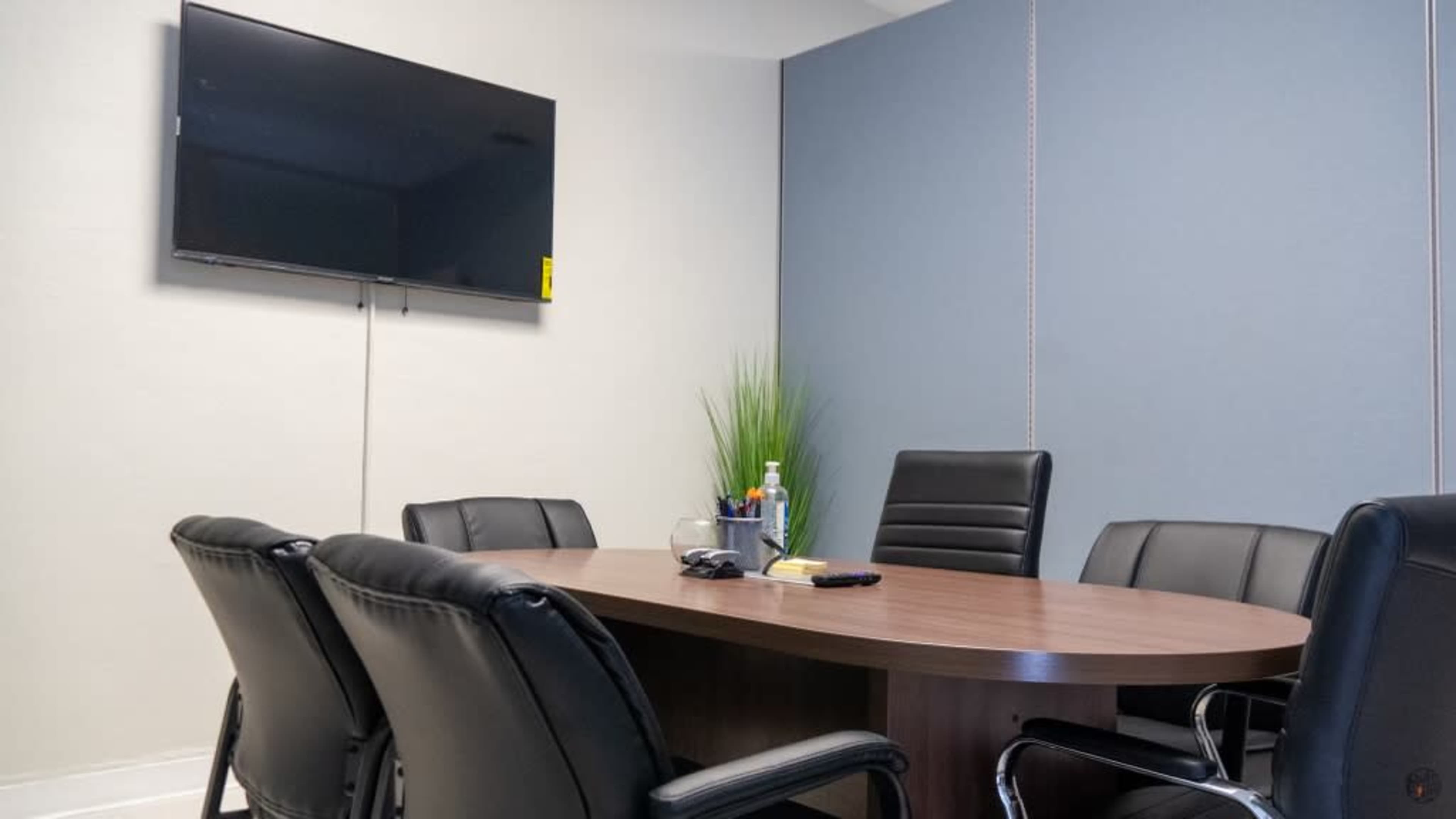 A conference room with a large wooden table, black leather chairs, and a wall-mounted television.