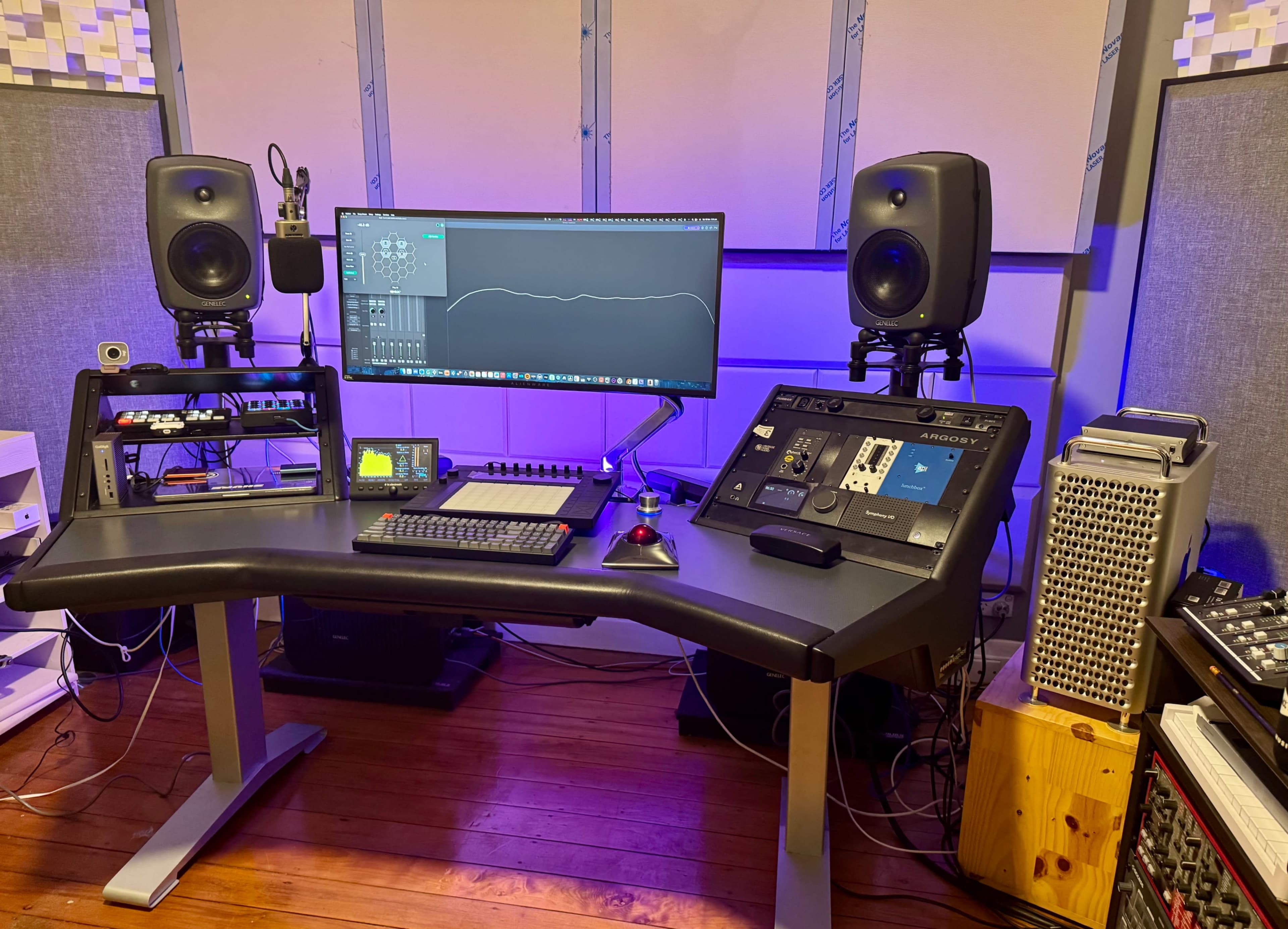 The image depicts a music production studio featuring a desk with a computer monitor, audio interface, speakers, and various audio equipment.