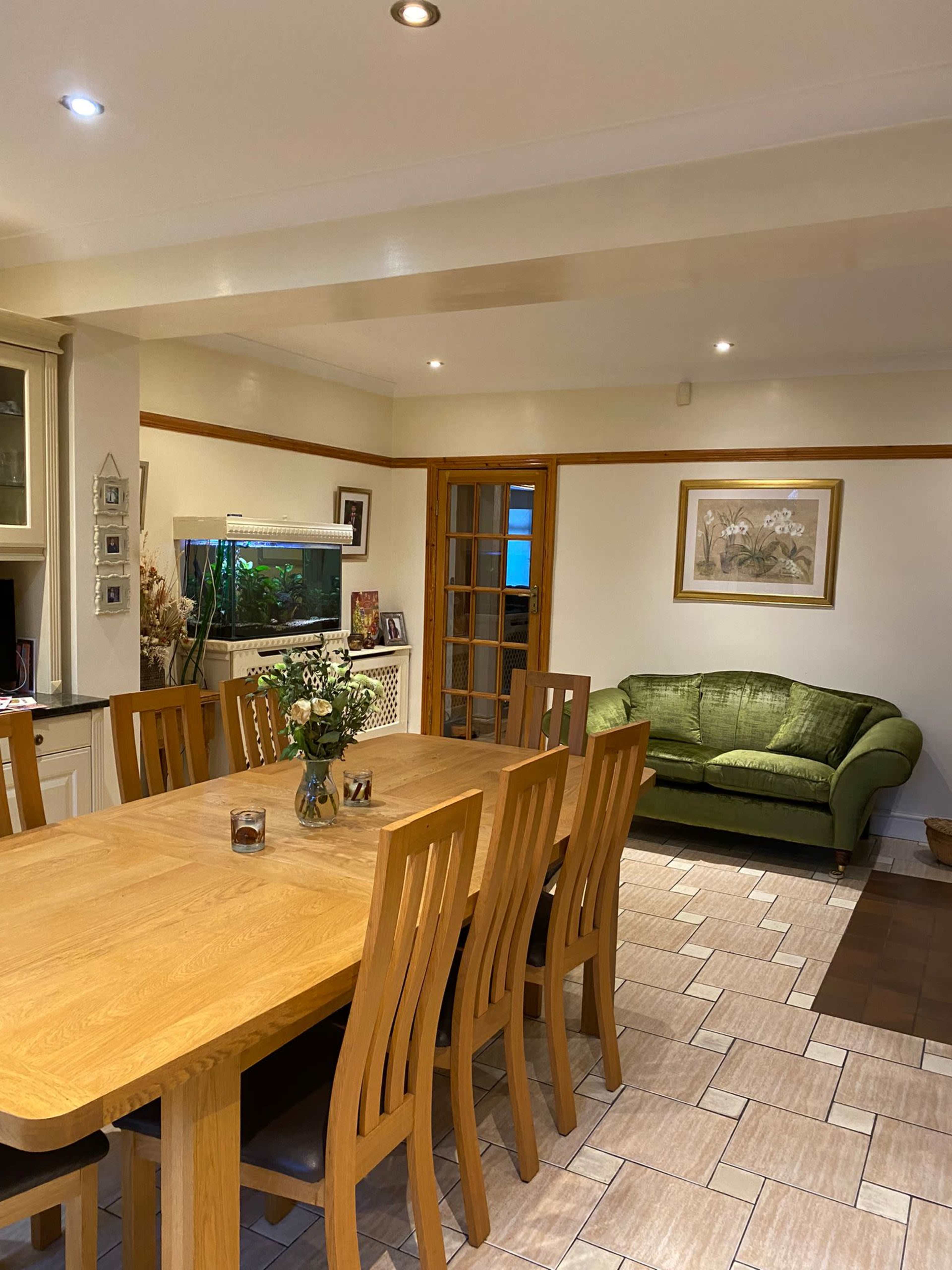 A dining area features a wooden table surrounded by chairs, an aquarium, and a green sofa in a well-lit room.