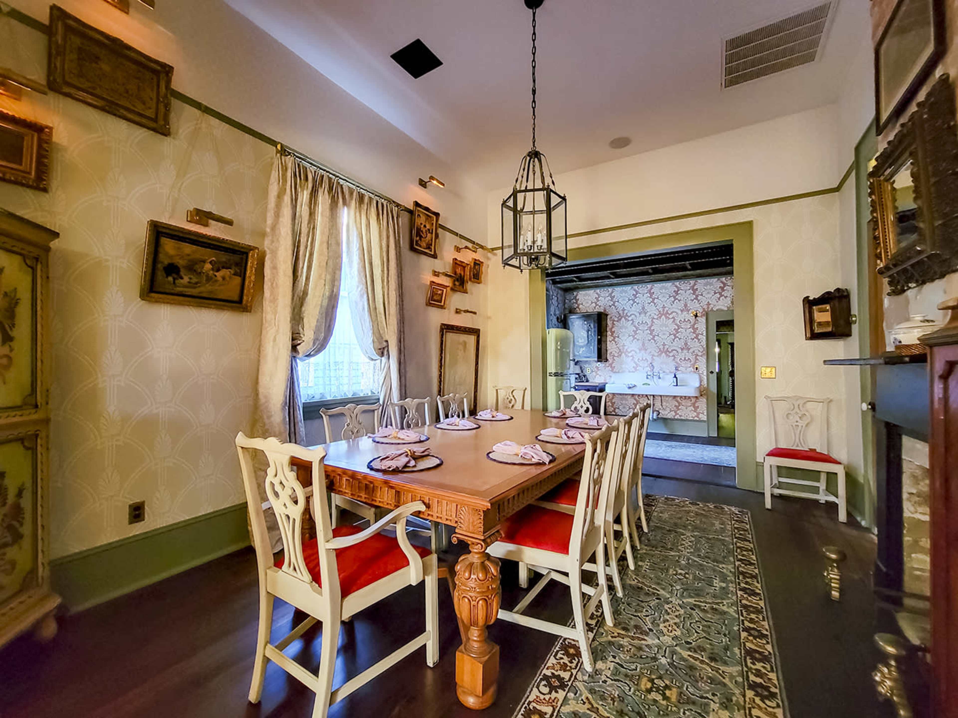 A dining room with a long wooden table set for a meal, surrounded by intricately decorated walls and vintage furnishings.