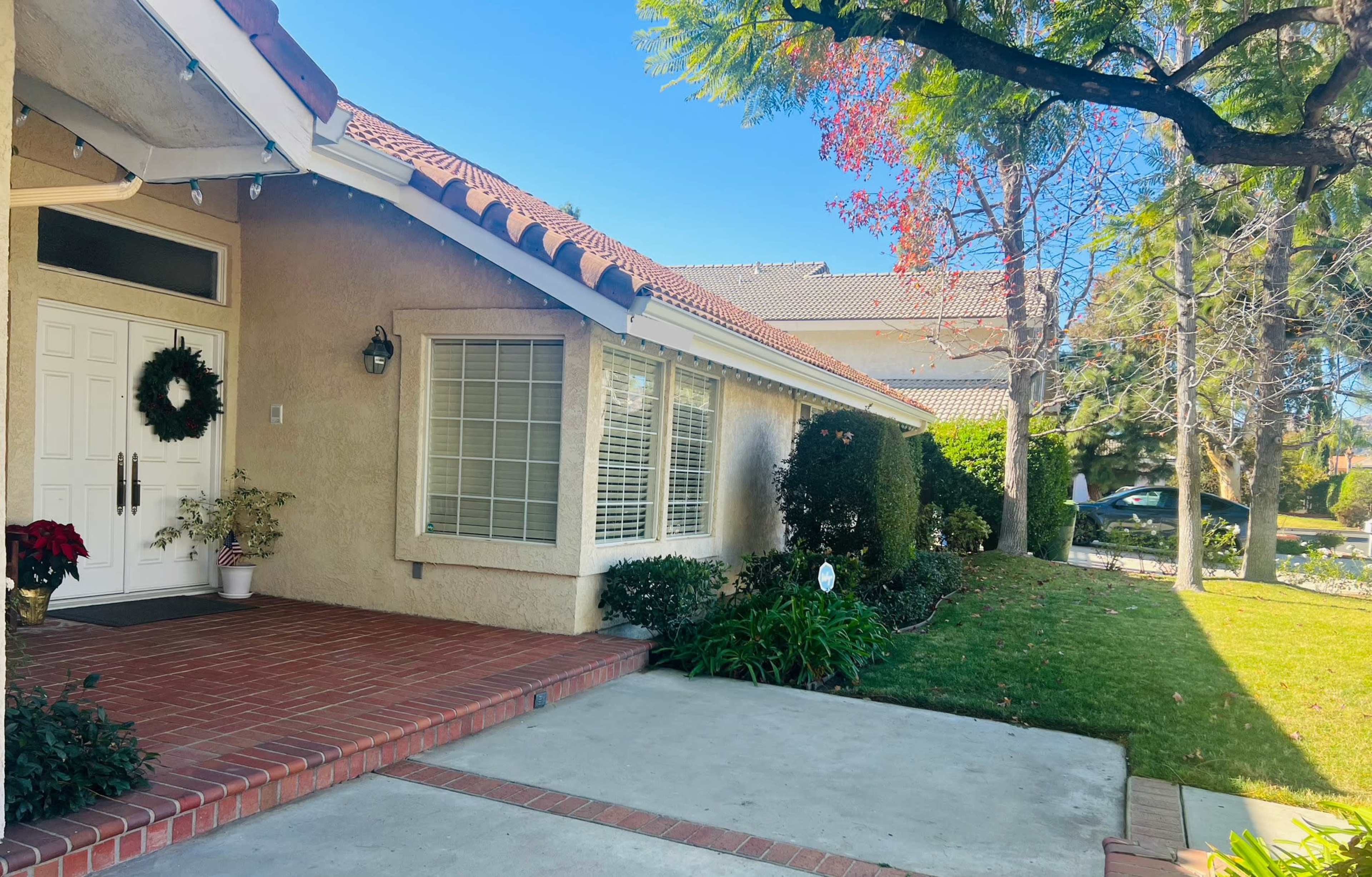 The entrance of a single-story house with a brick pathway, a holiday wreath on the door, and a landscaped front yard.