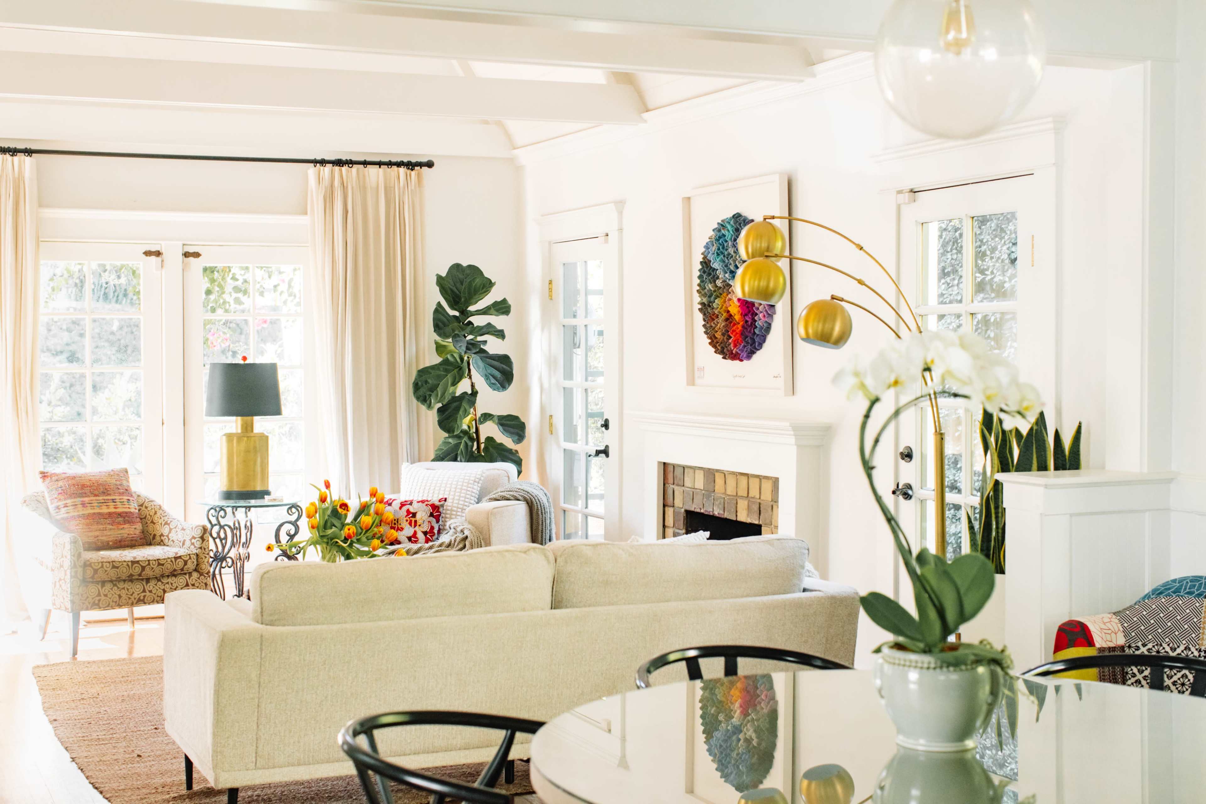 A bright living room with a beige sofa, a coffee table, indoor plants, and large windows letting in natural light.