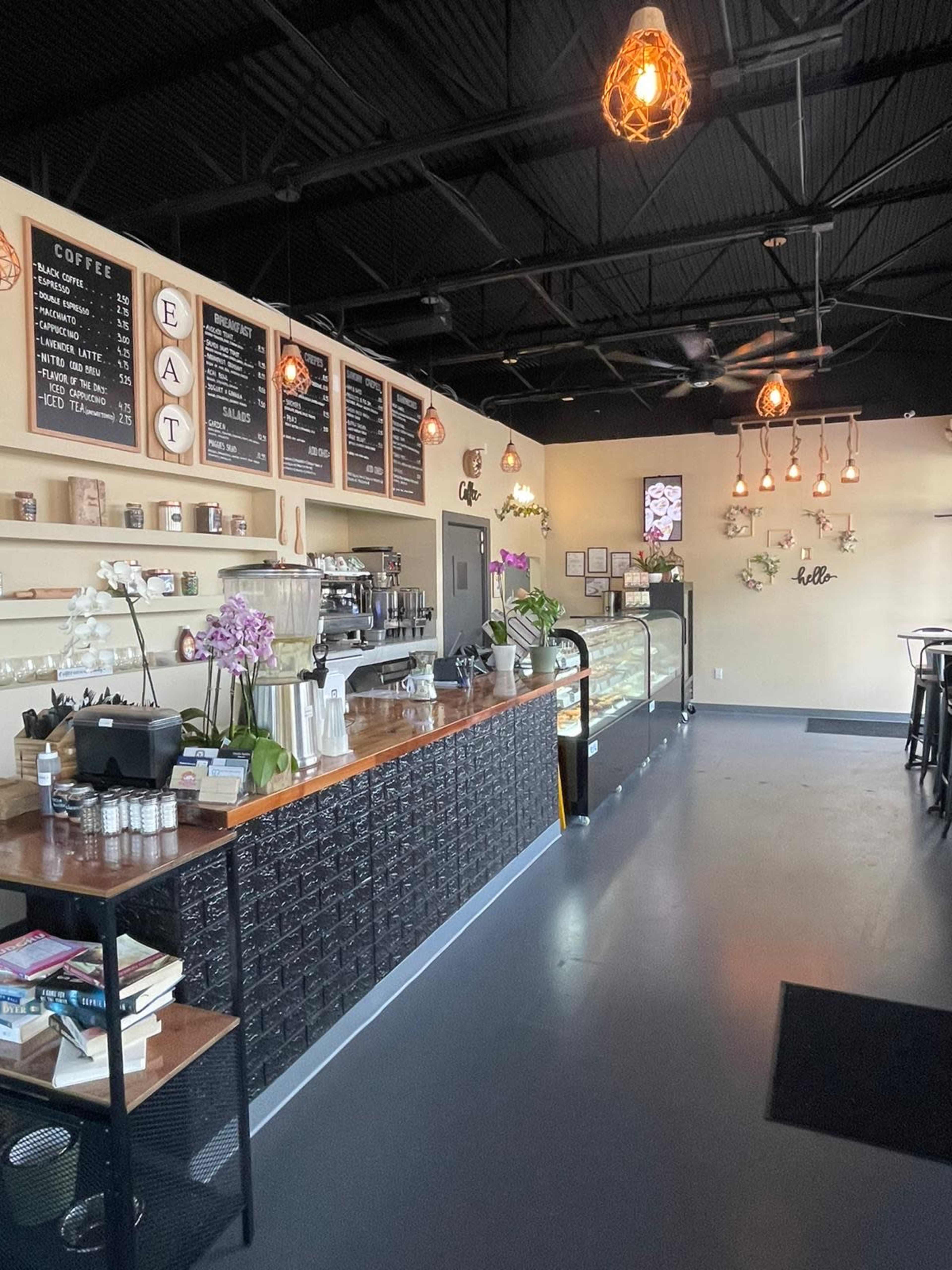 A coffee shop interior featuring a wooden counter with a display case, a menu on the wall, and decorative lighting fixtures hanging from the ceiling.