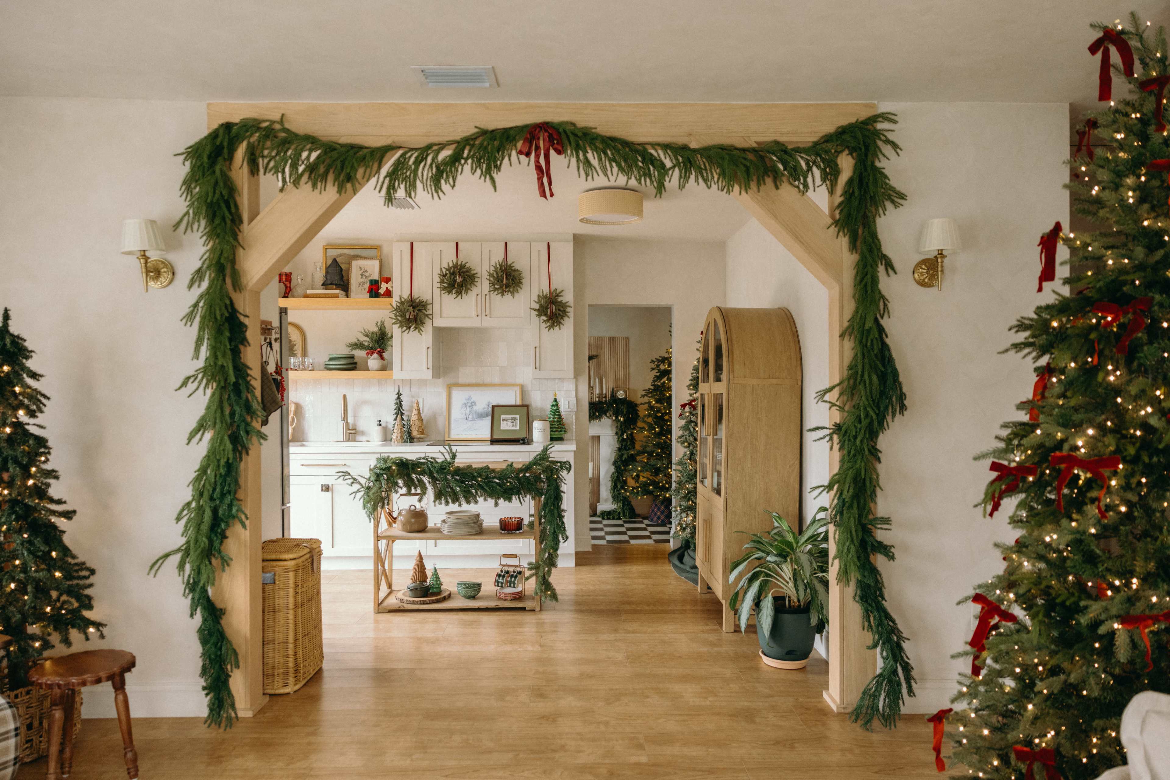 A decorated living space features garlands and Christmas trees, with a clear view of a kitchen at the back.