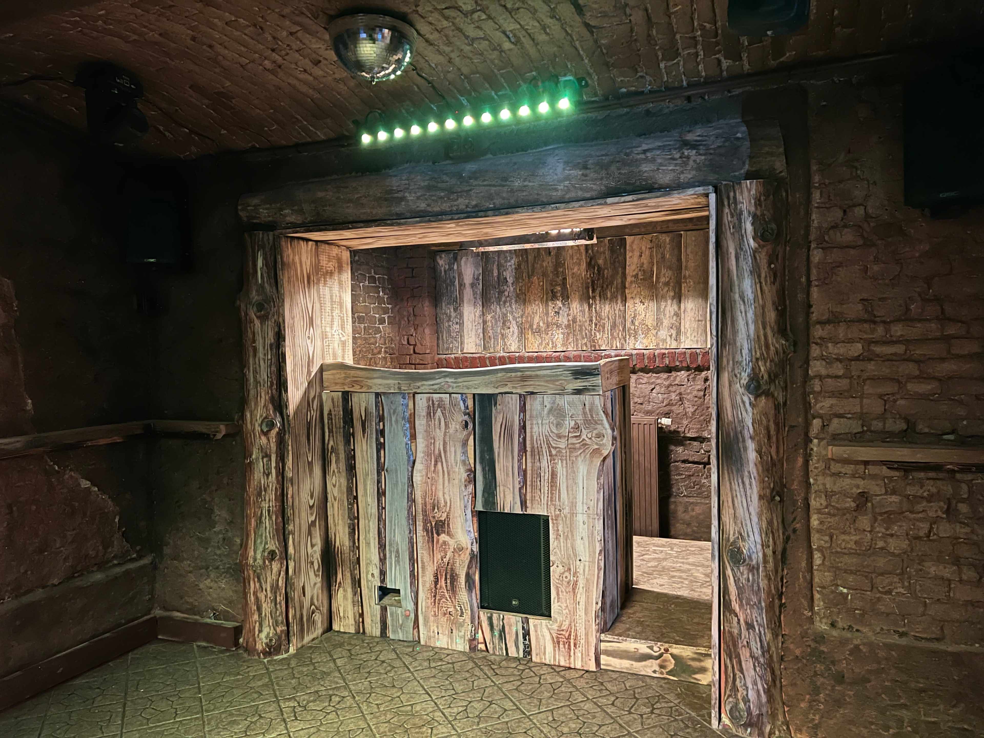 A wooden entrance leads into a dimly lit room with brick walls and a textured floor.