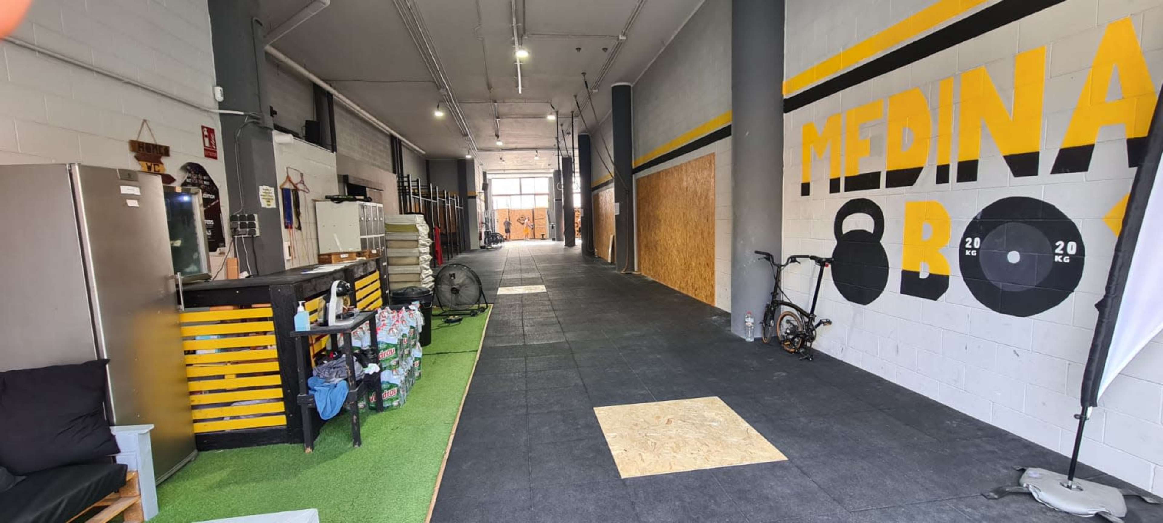 A fitness studio with exercise equipment, a small reception area, and a long, empty hallway featuring a large wall mural.
