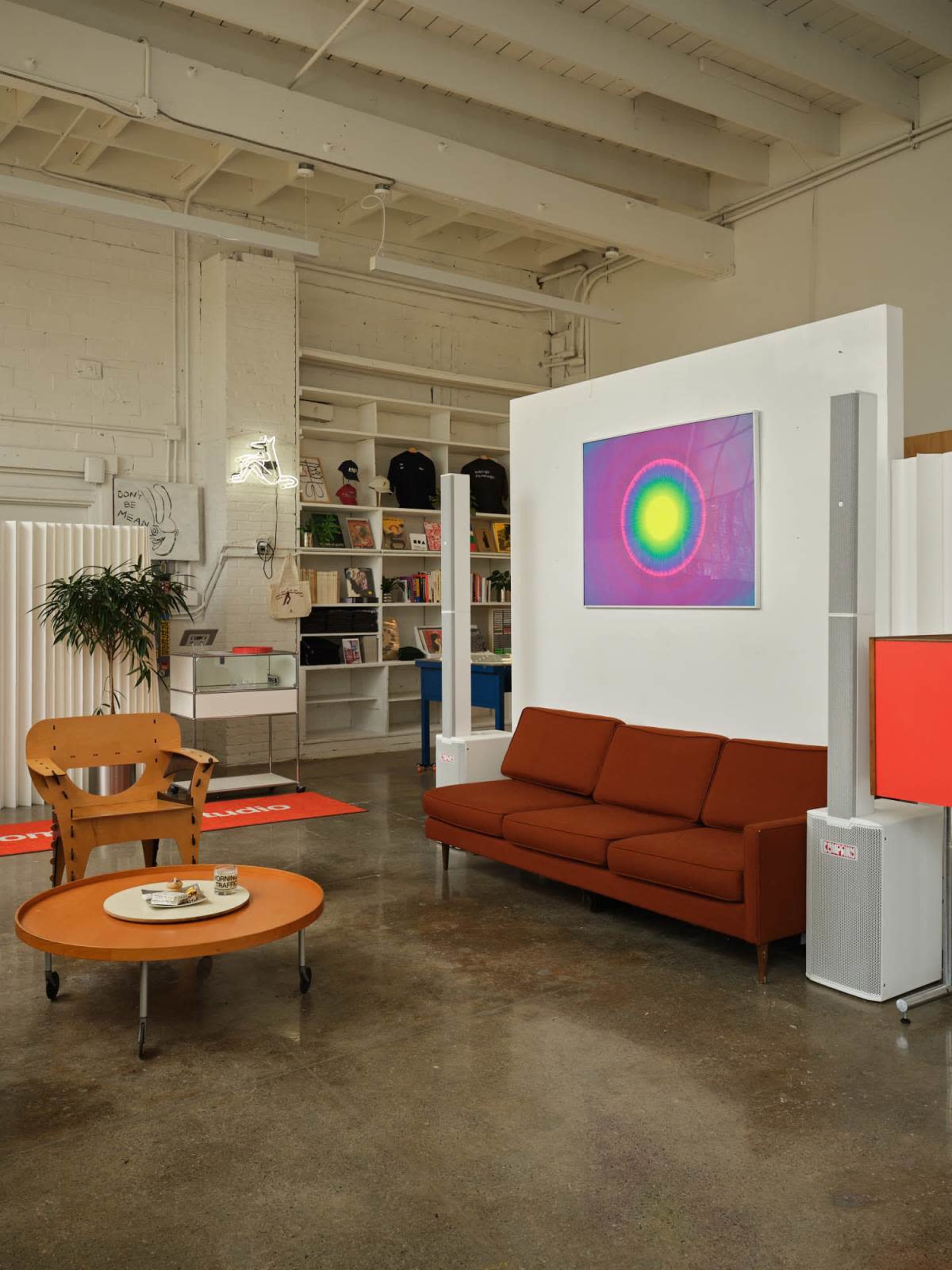 The image shows a modern, open living space featuring a brown sofa, a round coffee table with items on it, and a colorful artwork displayed on a white wall.