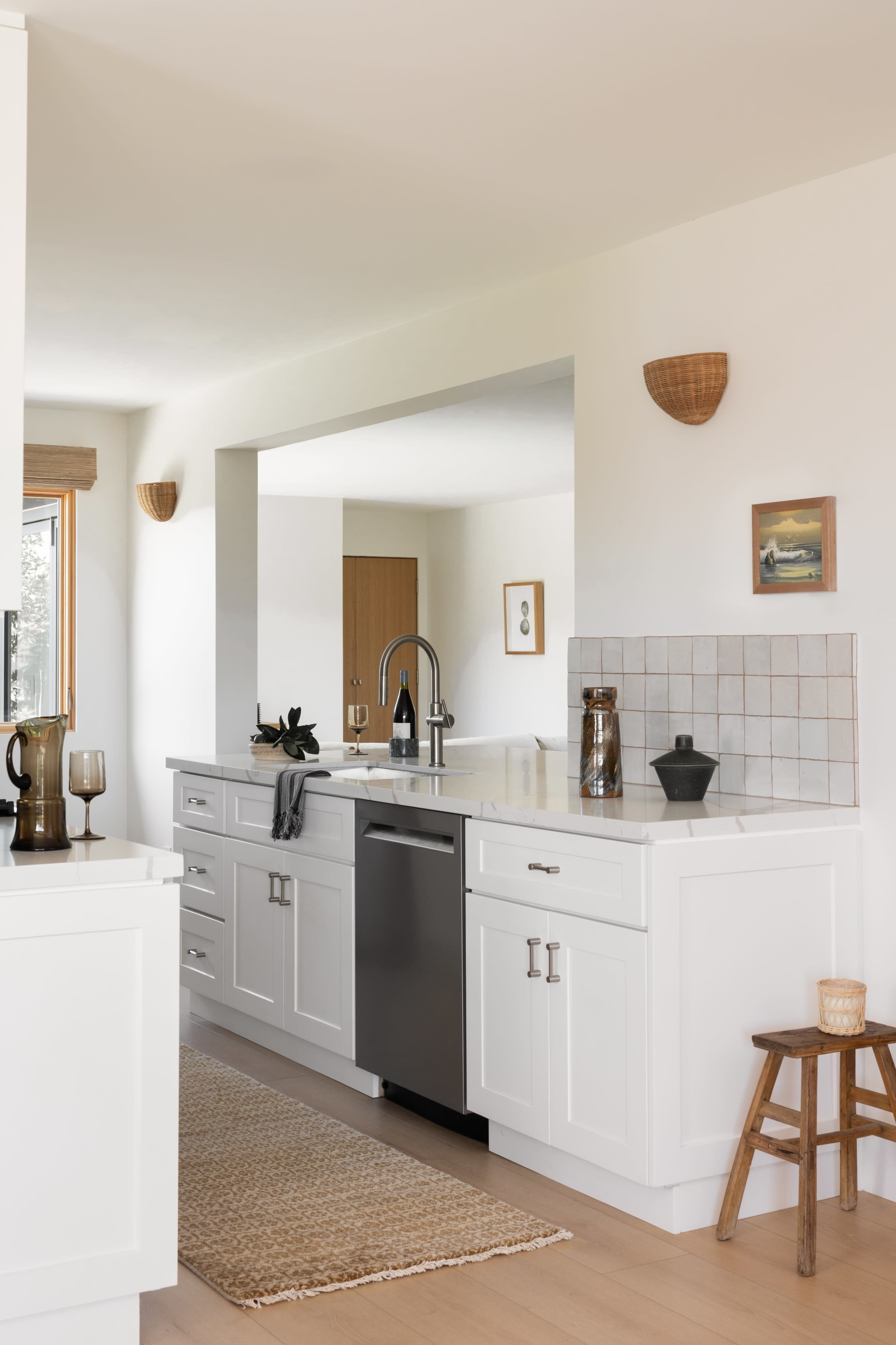The kitchen features white cabinetry, a stainless steel dishwasher, and a neutral-colored rug on hardwood flooring.
