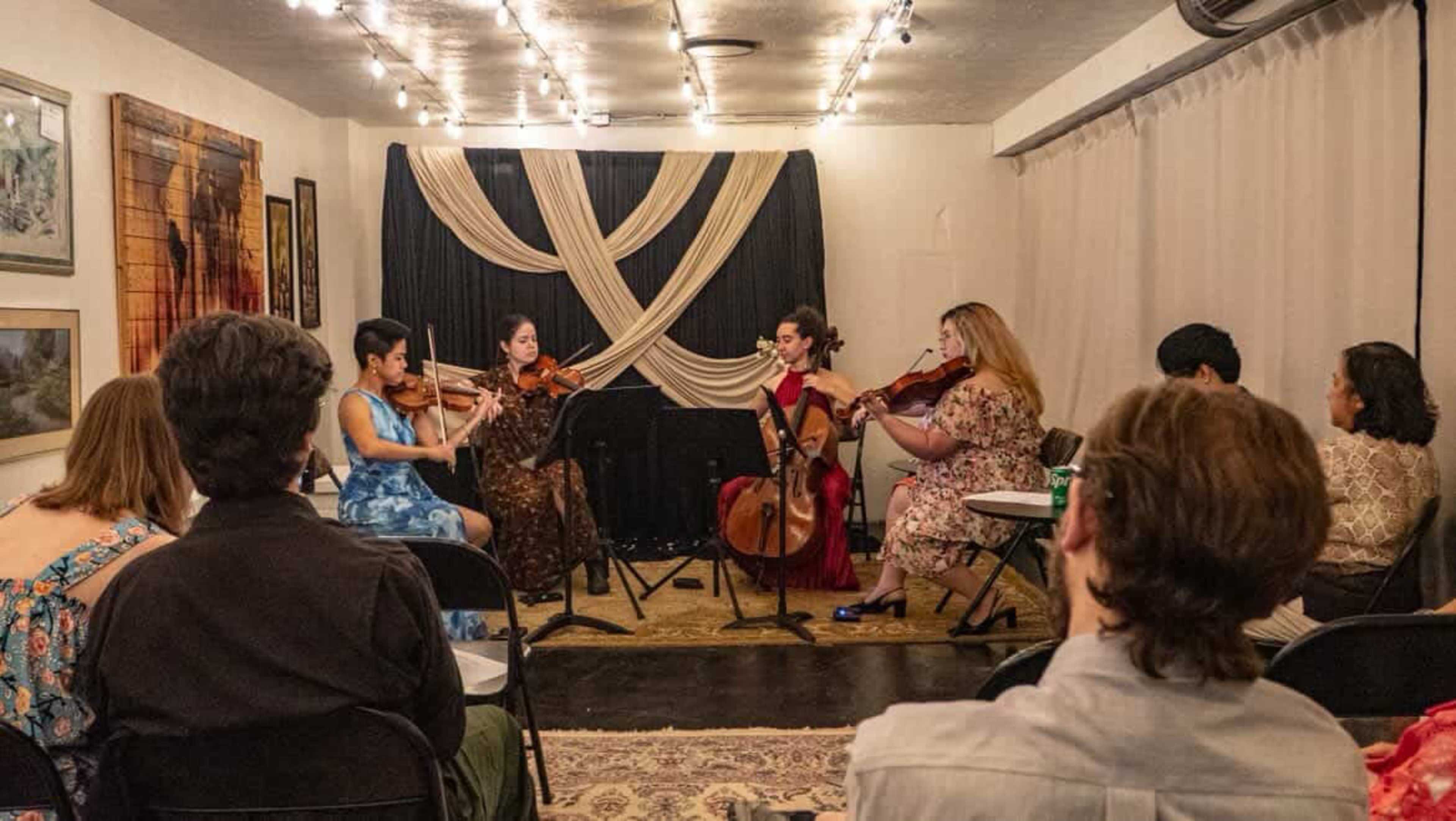 A string quartet performs in a small, intimate space with attendees seated in the foreground.