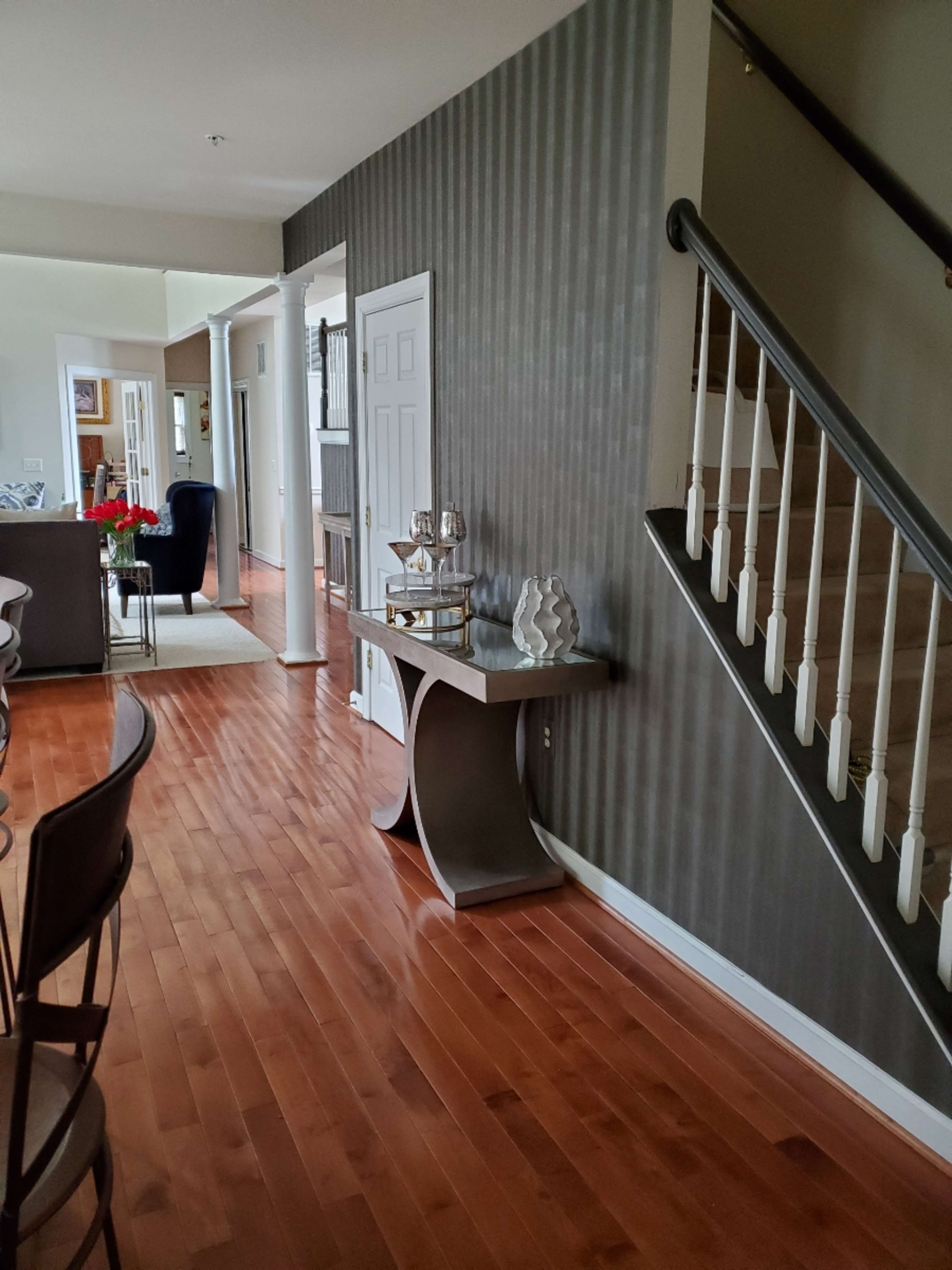 A hallway with hardwood floors, a decorative table against a striped wall, and a staircase leading to an upper level.