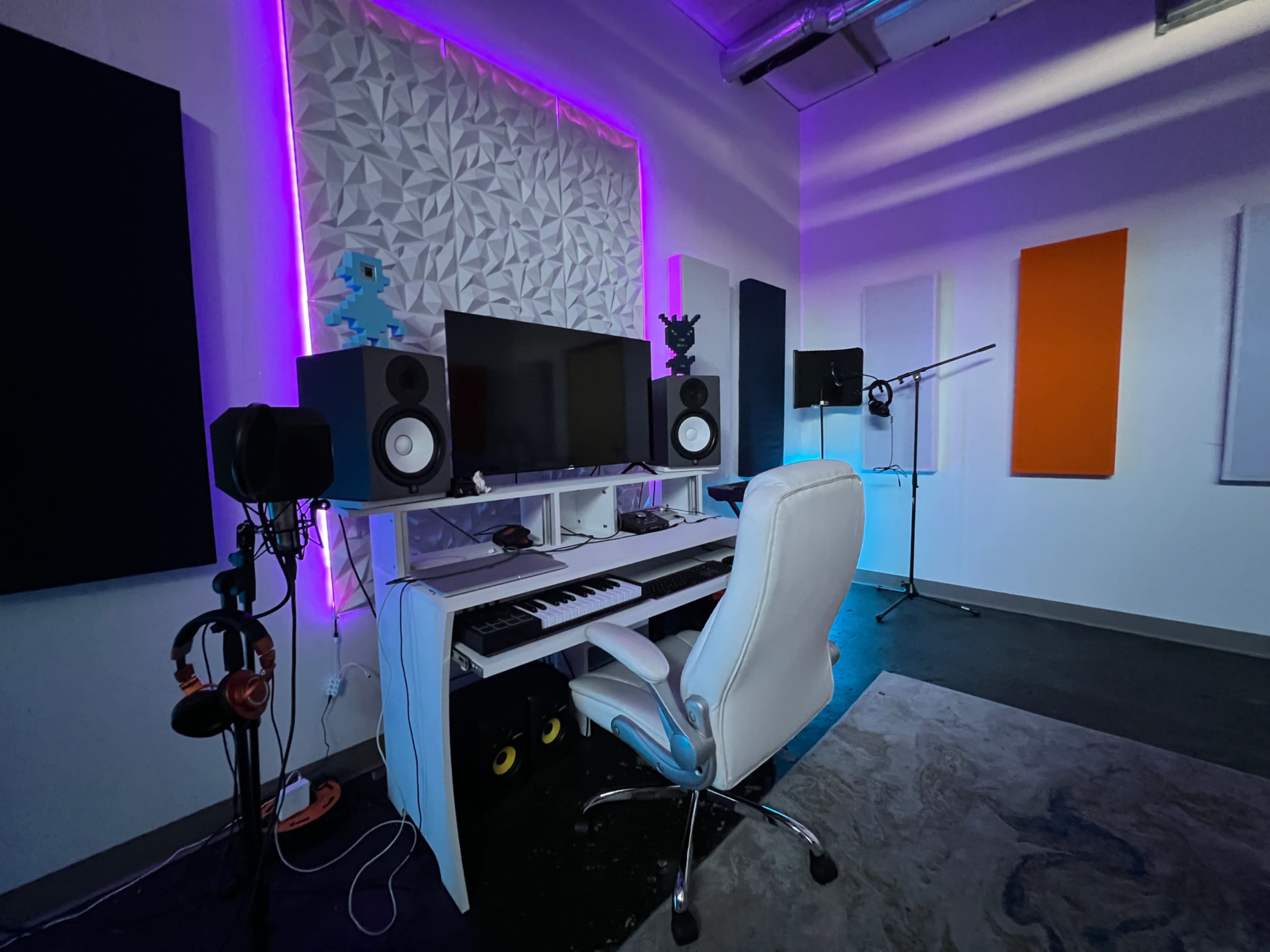 The image shows a music studio equipped with a keyboard, computer setup, and soundproof panels, illuminated by purple lighting.