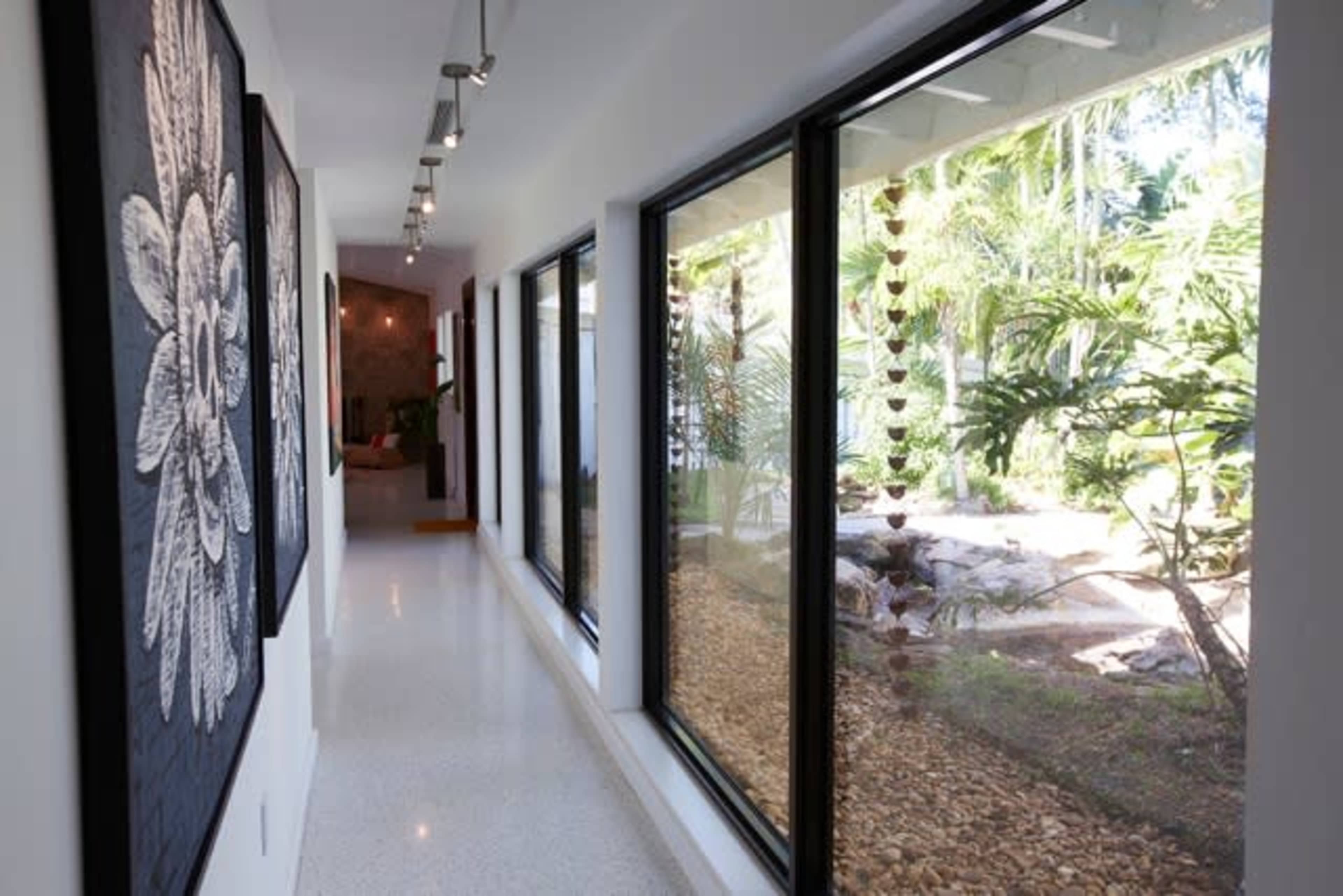 A modern hallway with large windows overlooks a garden filled with plants and landscaping features.