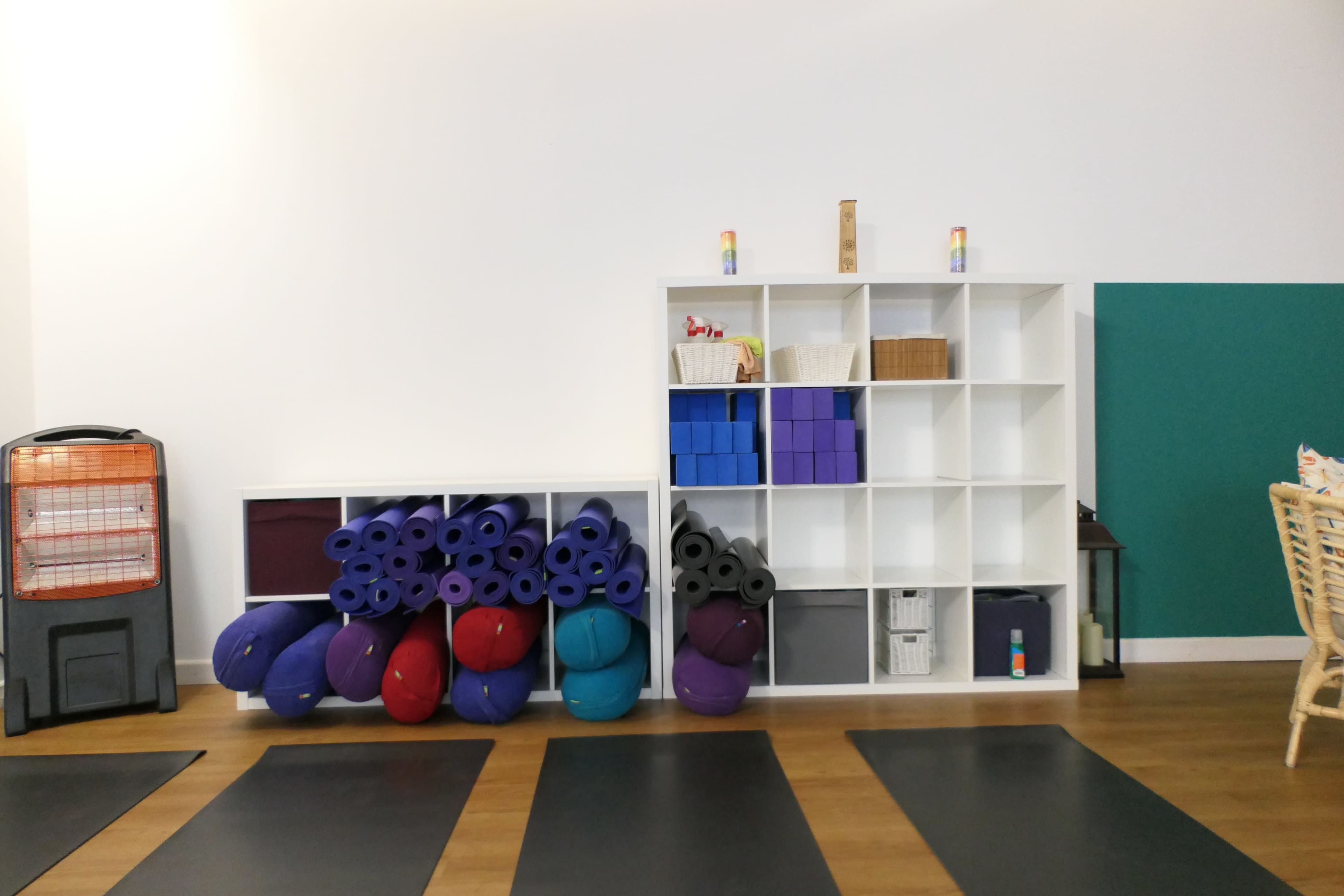 A fitness studio with neatly stacked exercise mats, balance balls, and a shelf containing various storage bins and supplies.