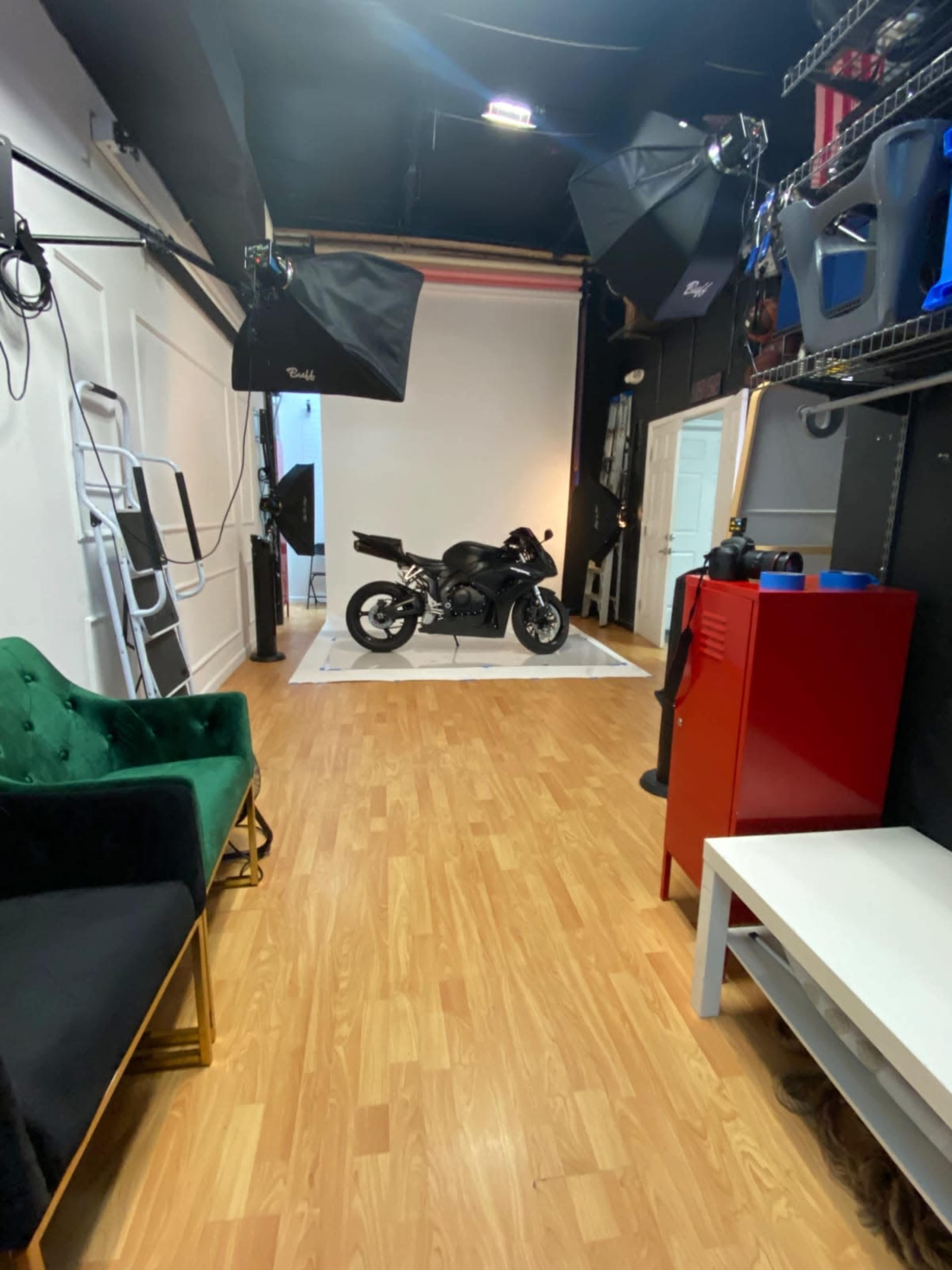 A spacious studio with a motorcycle displayed on a white platform, surrounded by studio lighting and various props.