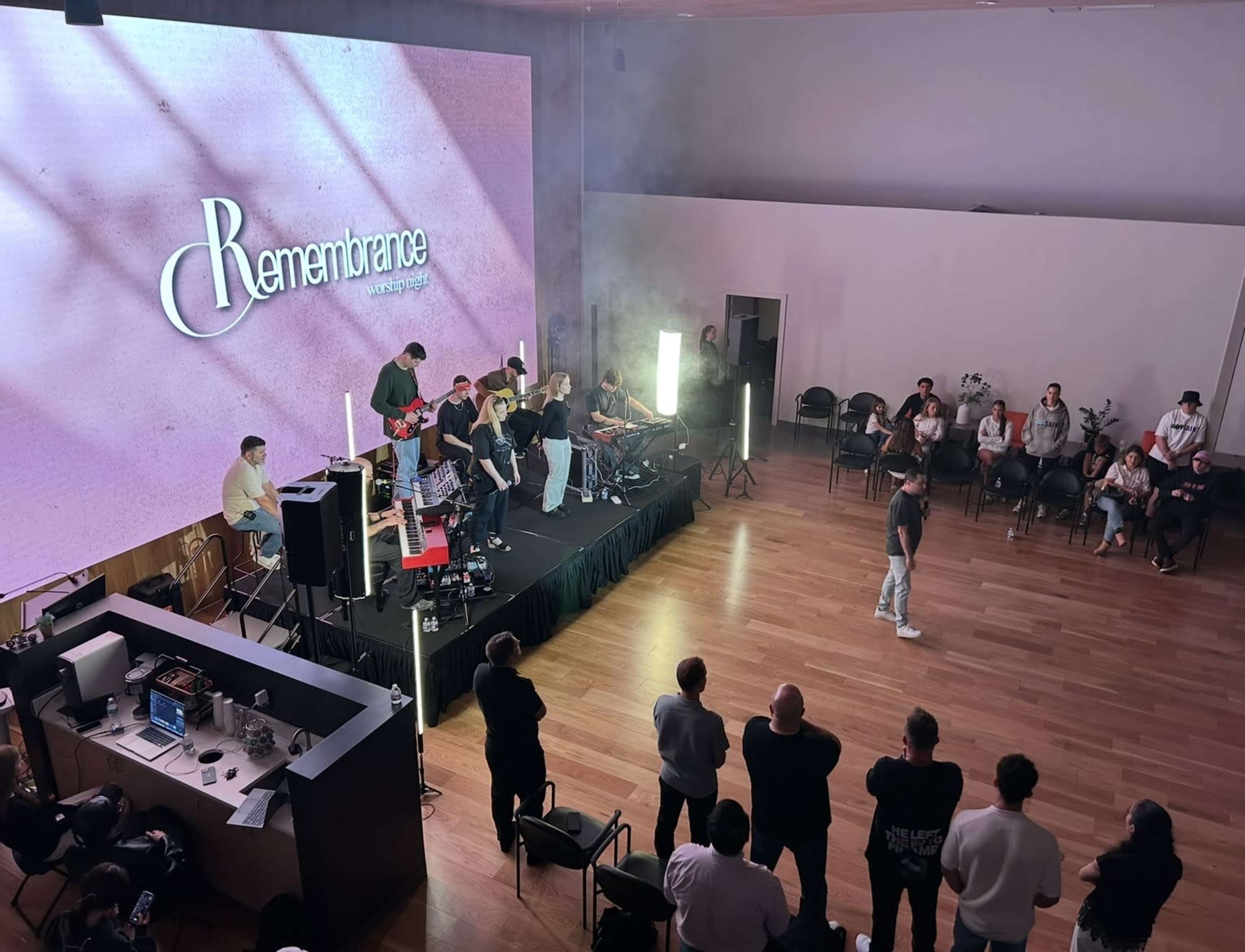 A live music performance is taking place on a stage with a large screen displaying the word "Remembrance" as an audience watches from below.