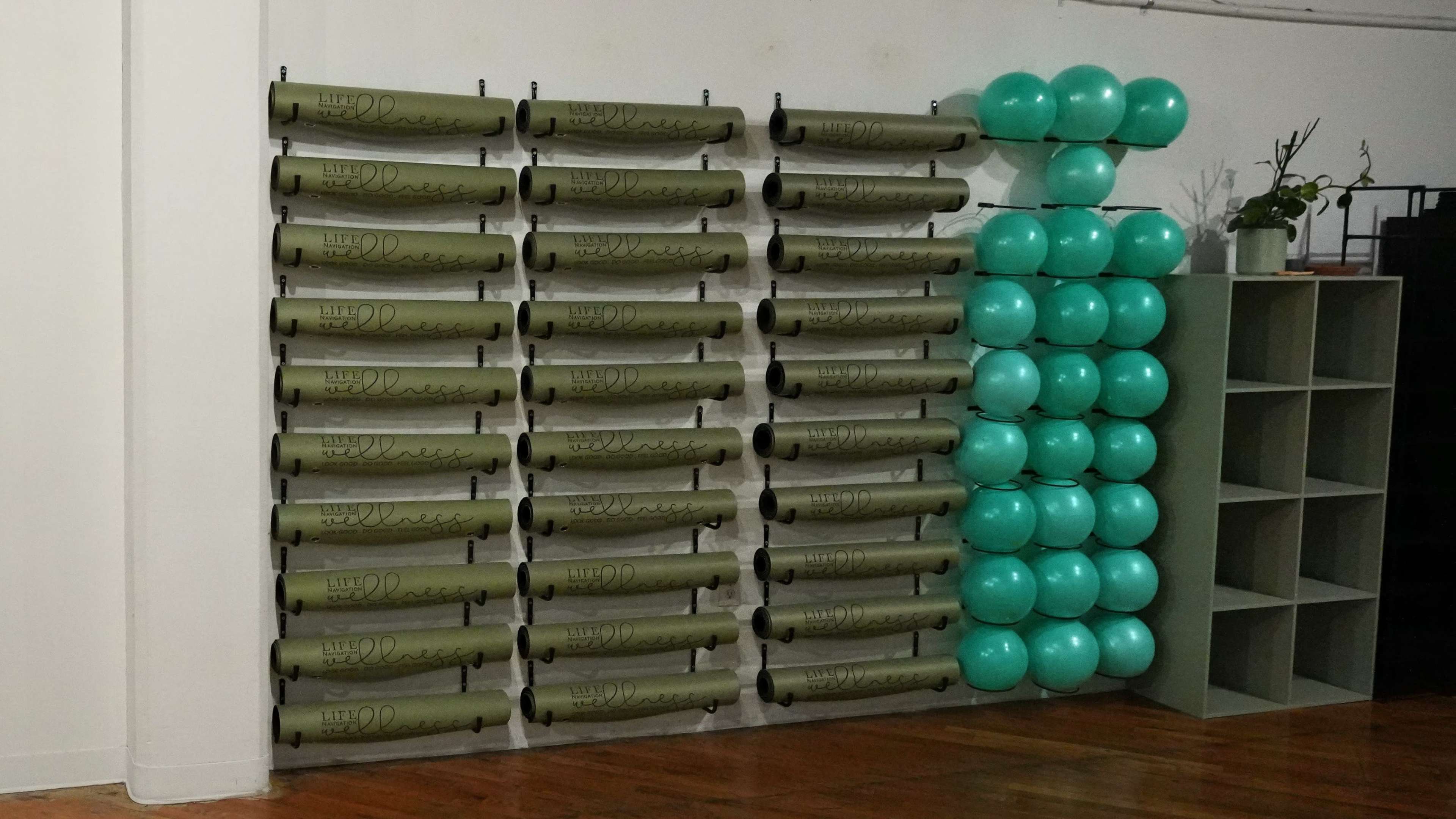 The image shows a wall lined with rolled yoga mats and a stack of turquoise exercise balls.