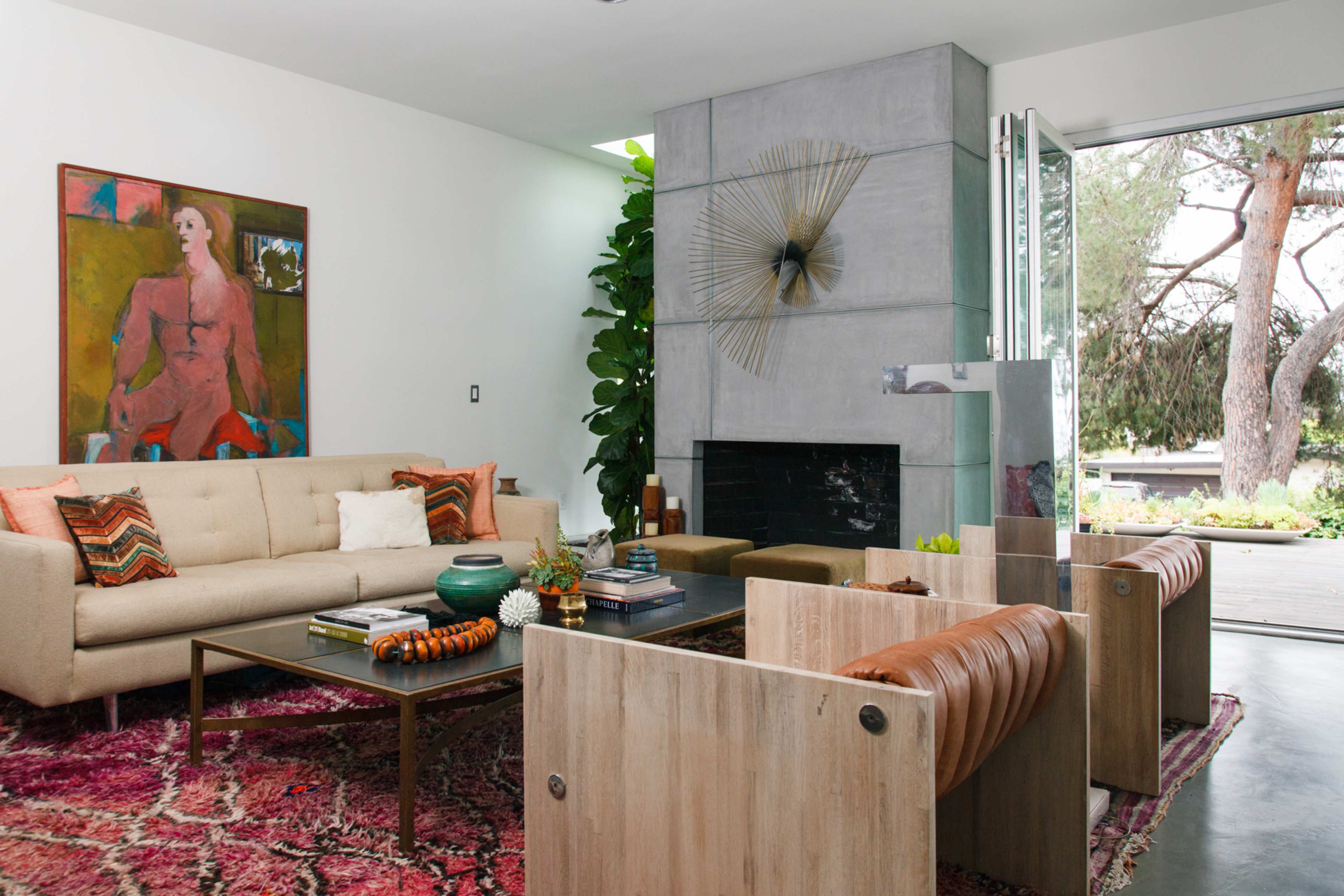 The living room features a light-colored sofa, wooden chairs, a coffee table, and a tall plant, with a painting on the wall and a fireplace.